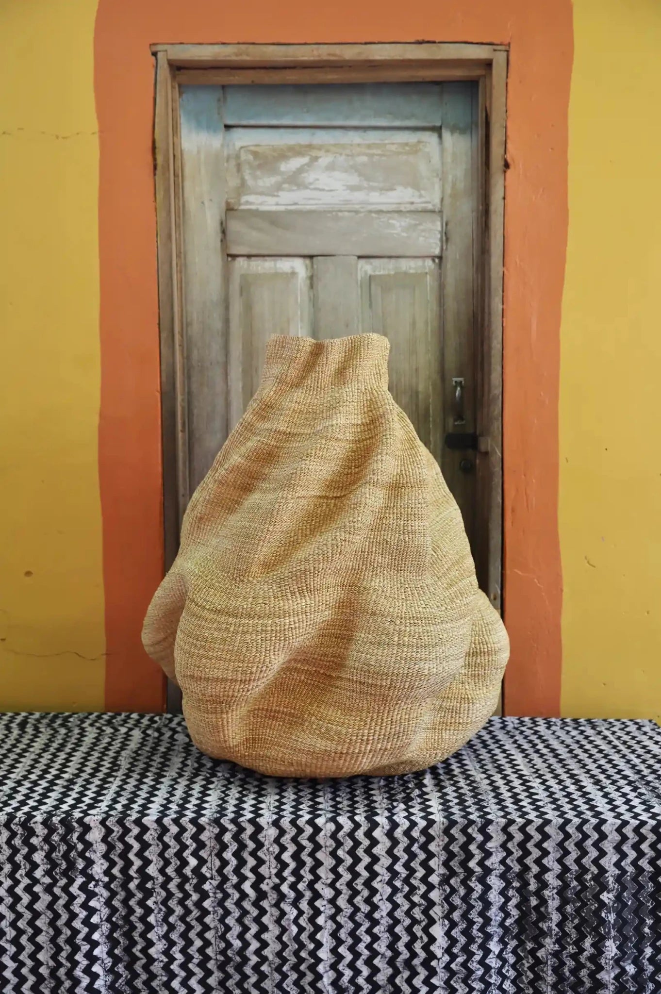 A  handwoven piece with decorative curves sitting on a black and white cloth against a wooden door