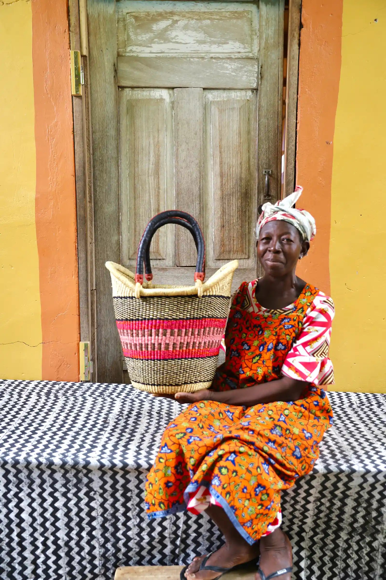 Artisan holding a colorful woven carry on bag with premium leather handles on a black and white cloth against a wooden door.