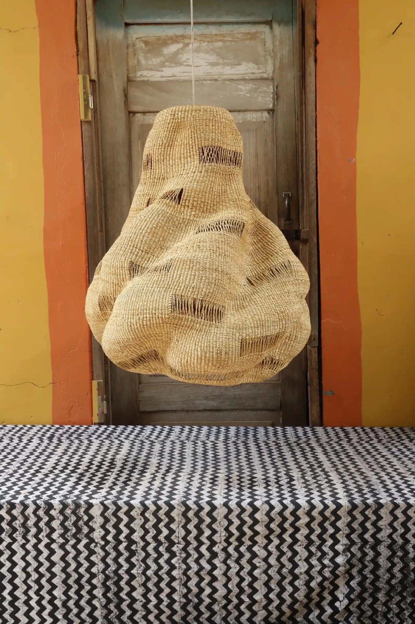 Woven bag hanging on a door with a patterned tablecloth in the foreground