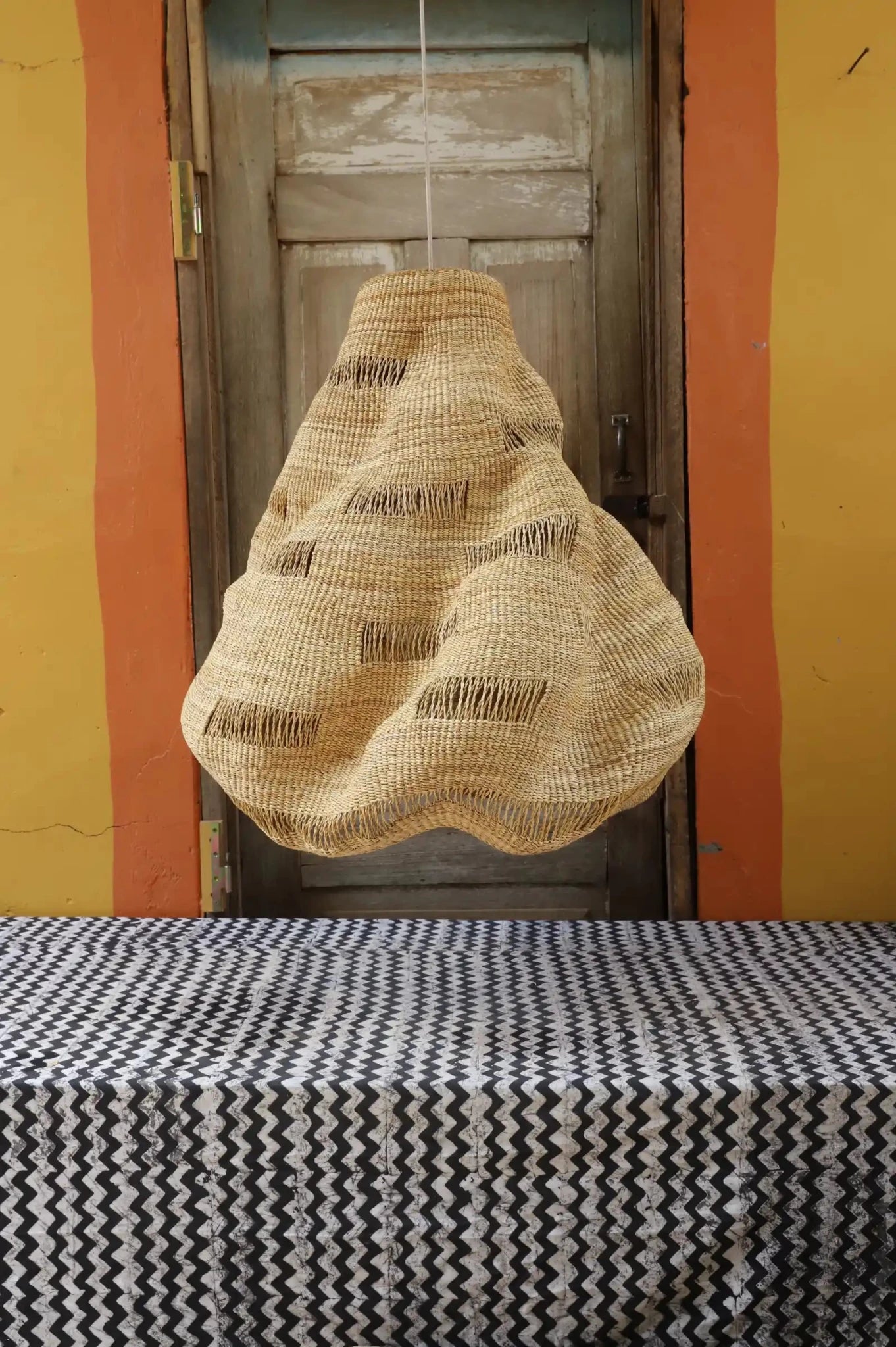 Woven basket hanging above a table with a patterned tablecloth against a yellow wall.