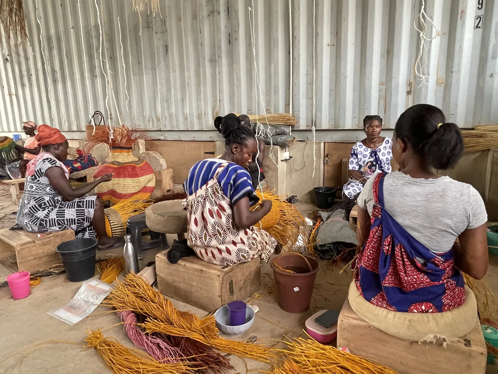 Baba Tree weavers working on baskets together, with straw and woven forms around them.