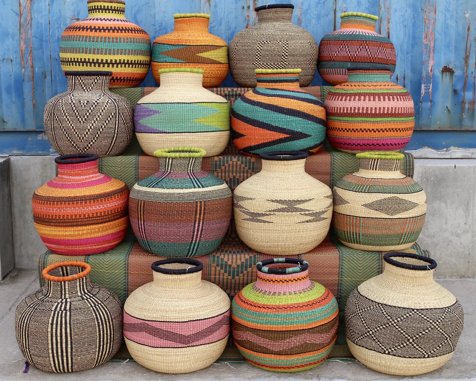 A group of colourful woven vessels arranged in rows against a blue doorway.
