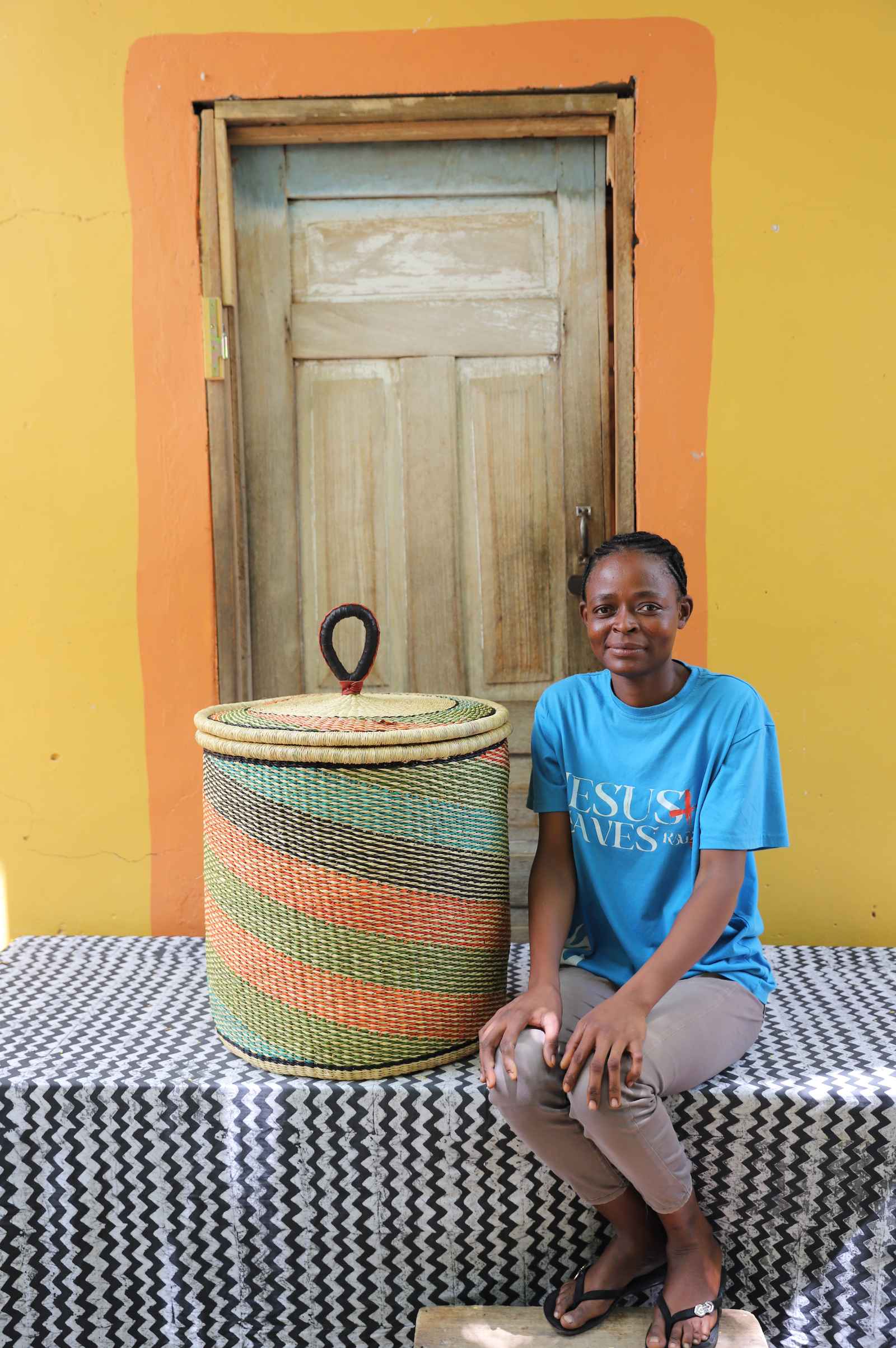 Handwoven Bolga laundry basket with fine multicolour diagonal stripes, beside a seated woman in blue.
