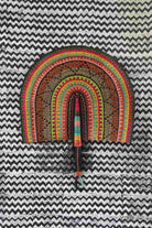 Naba Penga wall fan in natural straw with black, green and orange banding, laid on a chevron cloth.