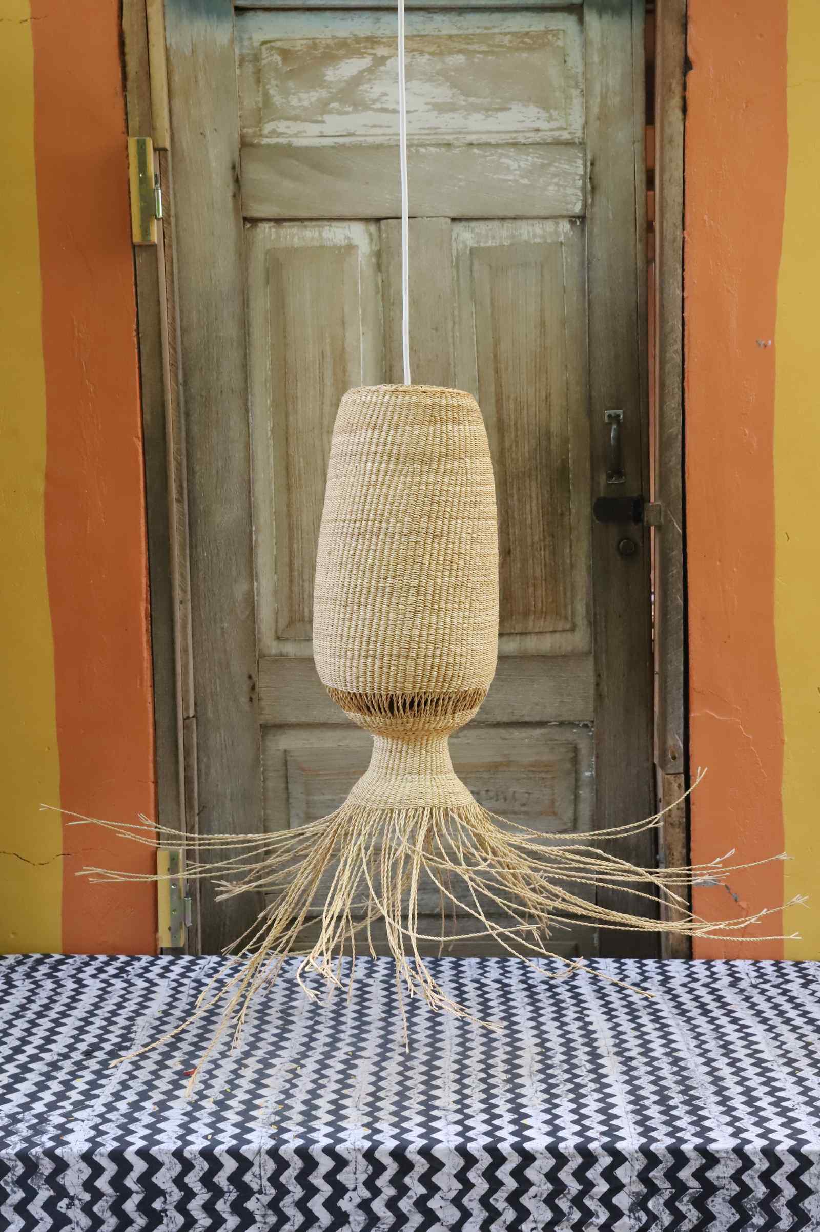 Abyssal pendant lampshade with long trailing fringe, hanging before a weathered wooden door.