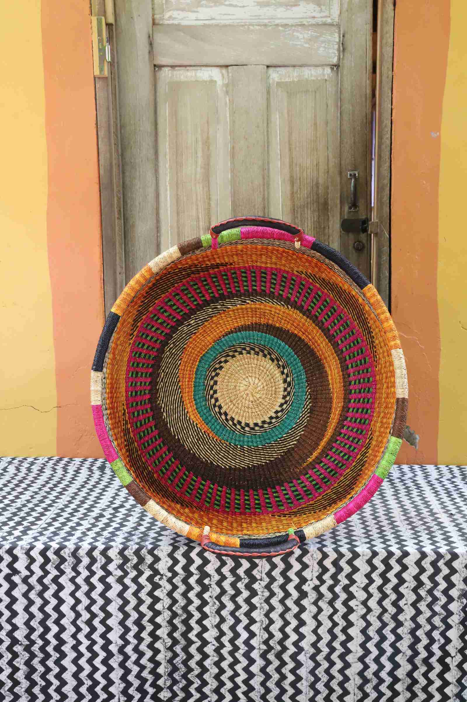 Large handwoven Bolga wall tray disc with bright orange, pink, purple and teal concentric bands.