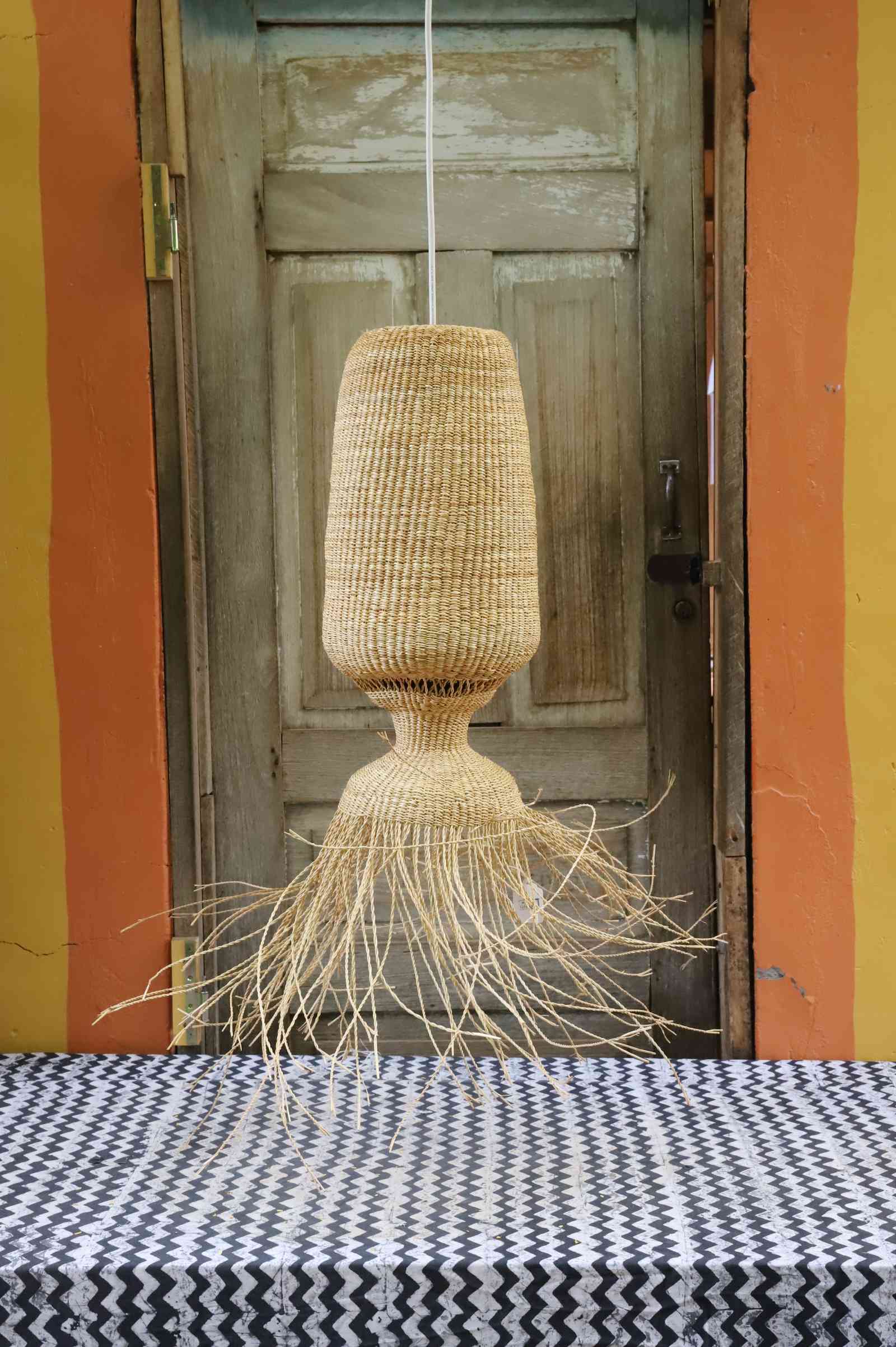 Abyssal pendant lampshade with a wide fringed base, hanging in front of a weathered wooden door.