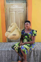 Woman in a floral dress seated beside the Cosma pendant lampshade in a weathered doorway.