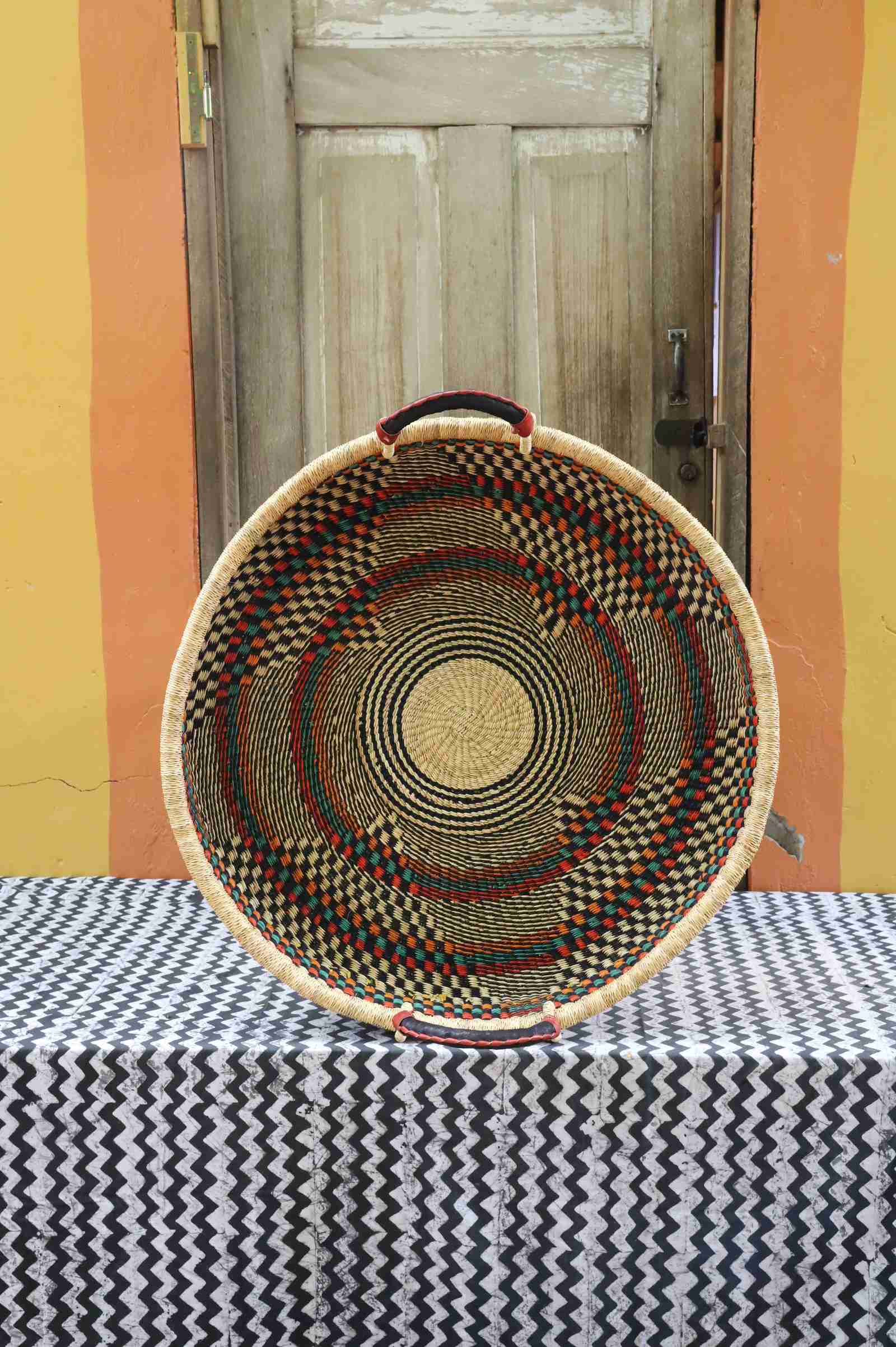 Large handwoven Bolga wall tray disc in natural straw with dark radial diamond and star pattern.