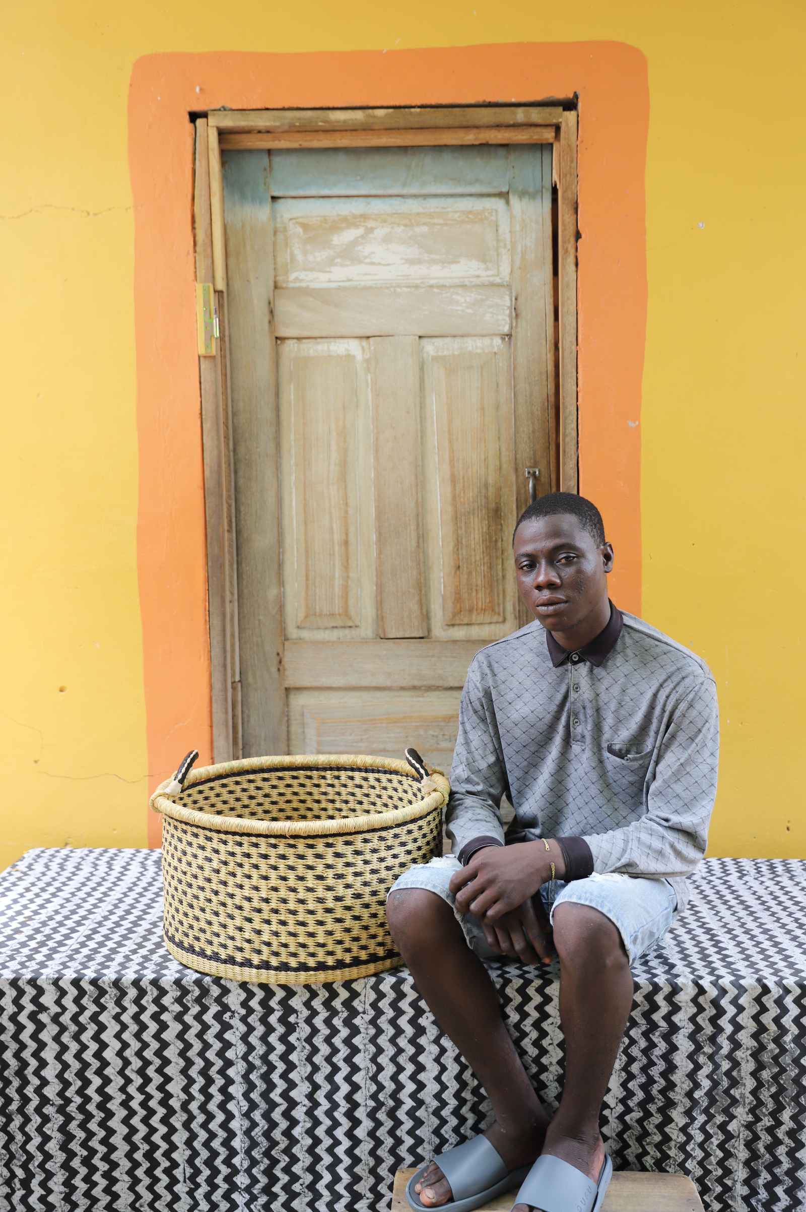 Medium handwoven Bolga storage tub in plain natural straw with dark handles, beside a seated man.