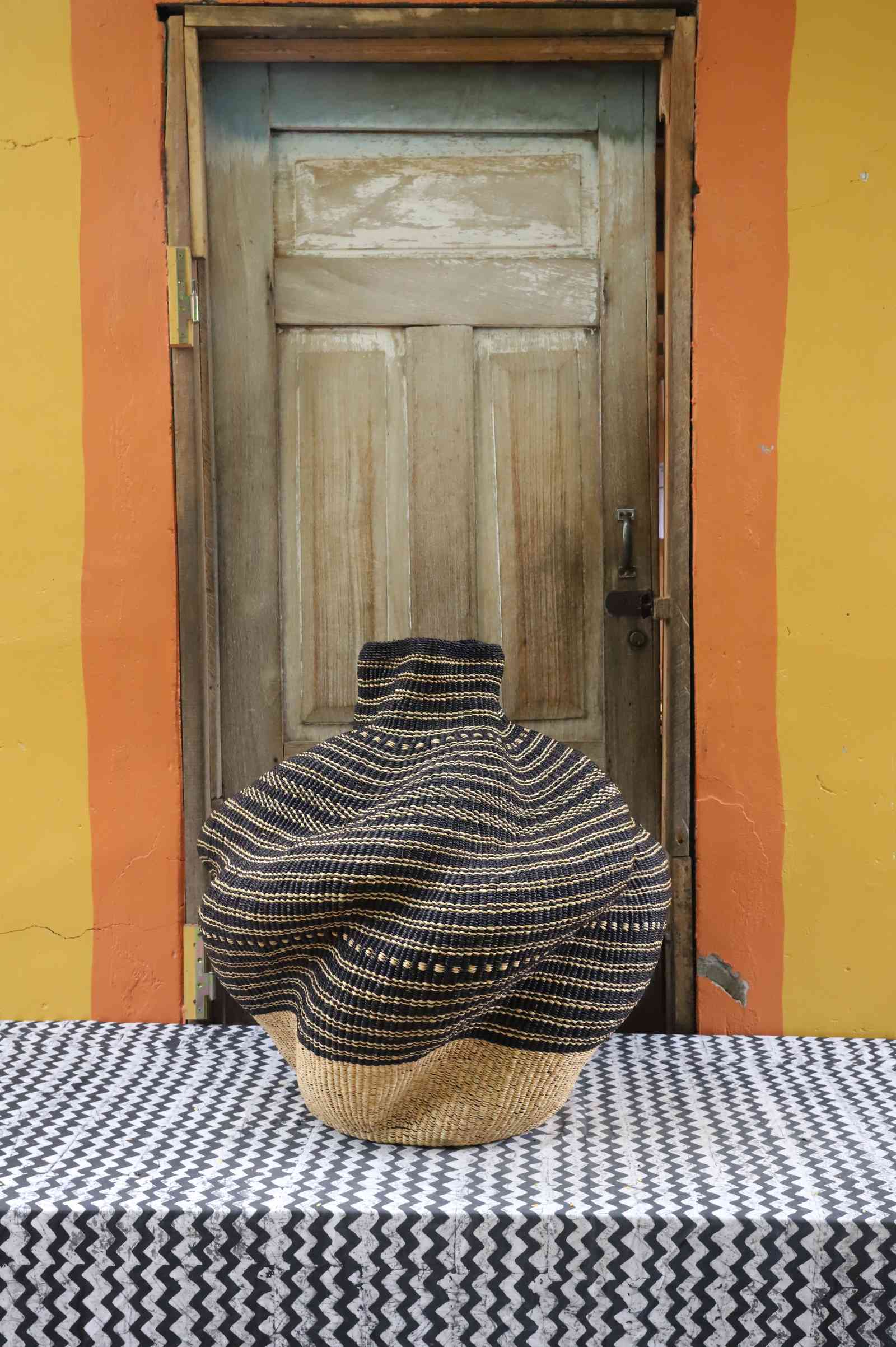 Medium handwoven Bolga art basket in natural straw with dark bands, side view of the sculpted lobed form.