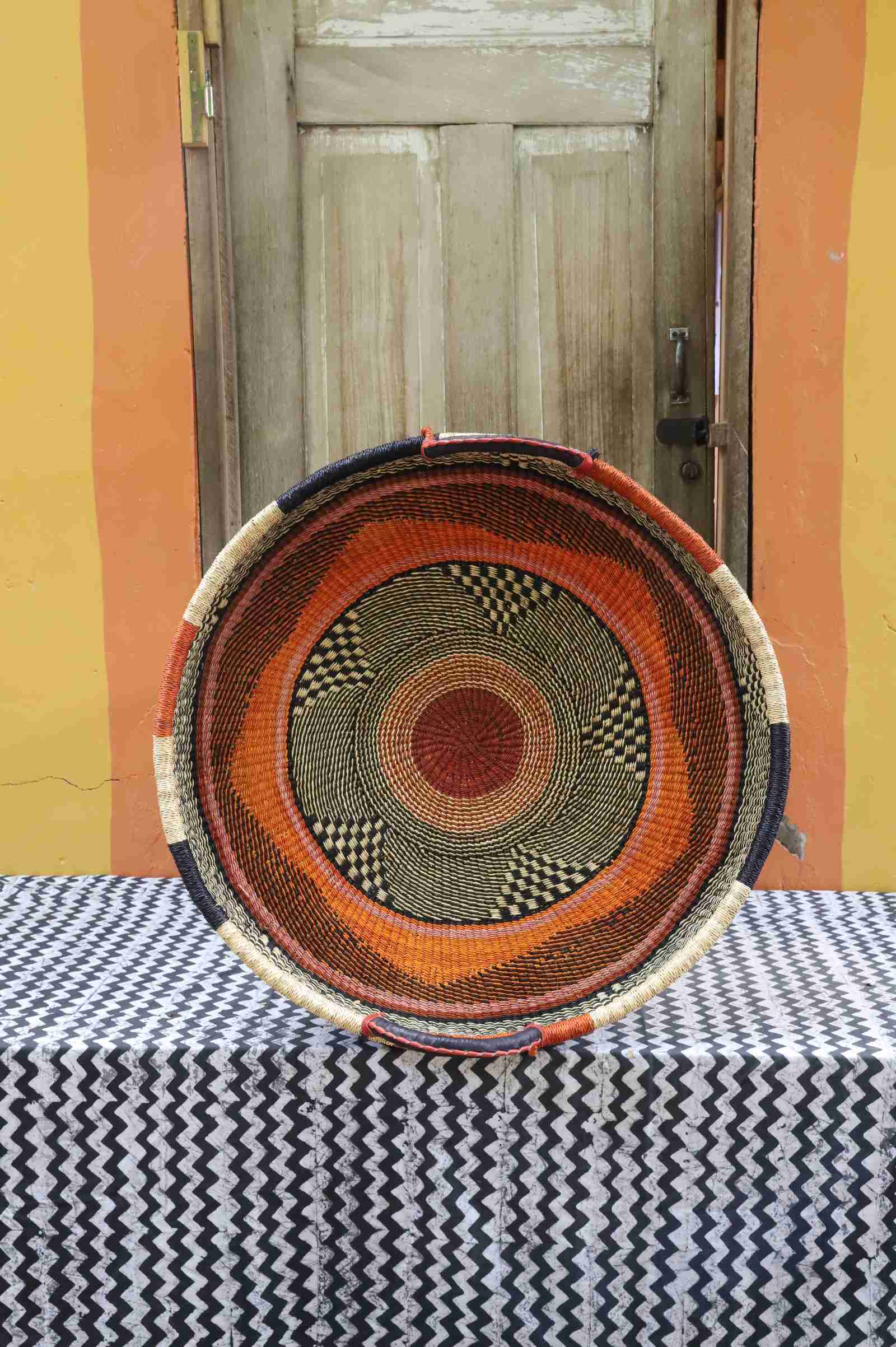 Large handwoven Bolga wall tray disc in natural straw with orange, black and red concentric bands.
