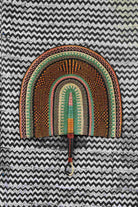 Naba Penga wall fan in natural straw with sage green and rust banded arches, laid on a chevron cloth.