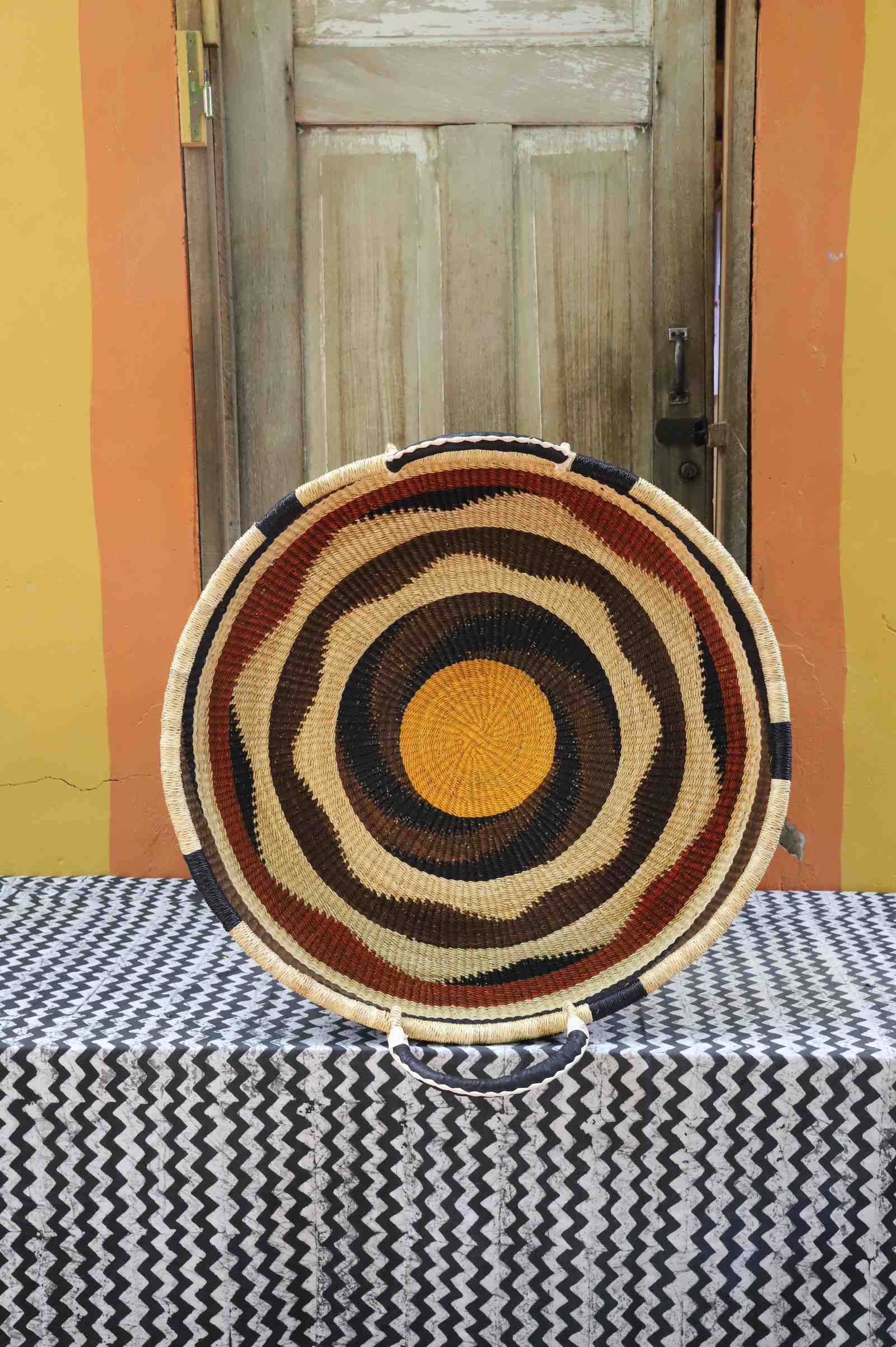 Large handwoven Bolga wall tray disc with brown, orange and tan concentric bands and a yellow centre.