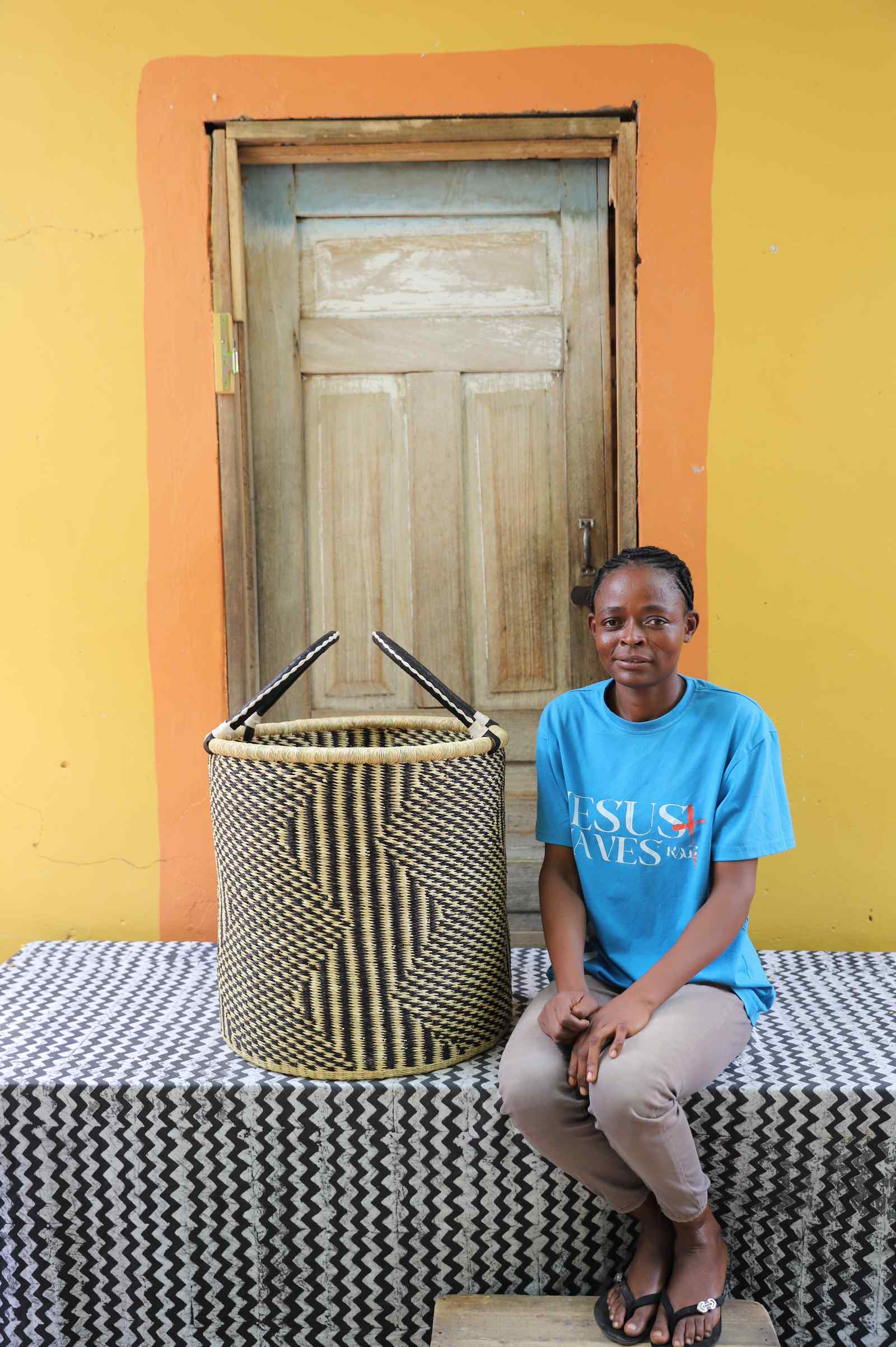 Large handwoven Bolga laundry basket in natural with fine black diamond weave, beside a seated woman in blue.