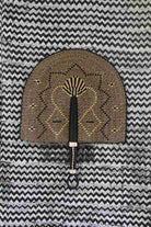 Naba Penga wall fan in dark brown straw with a tan star-shaped geometric weave, laid on a chevron cloth.