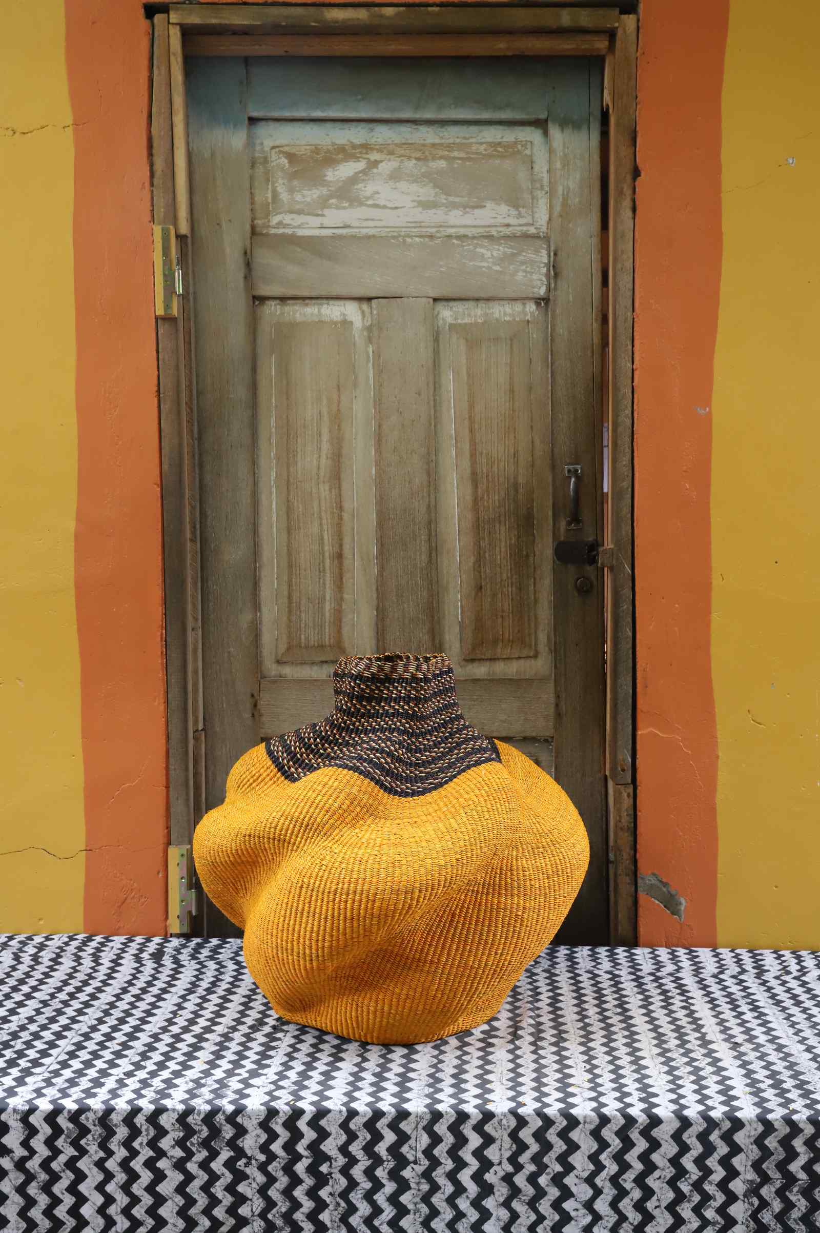 Medium handwoven Bolga art basket in mustard-yellow, side view of the sculpted lobed form.