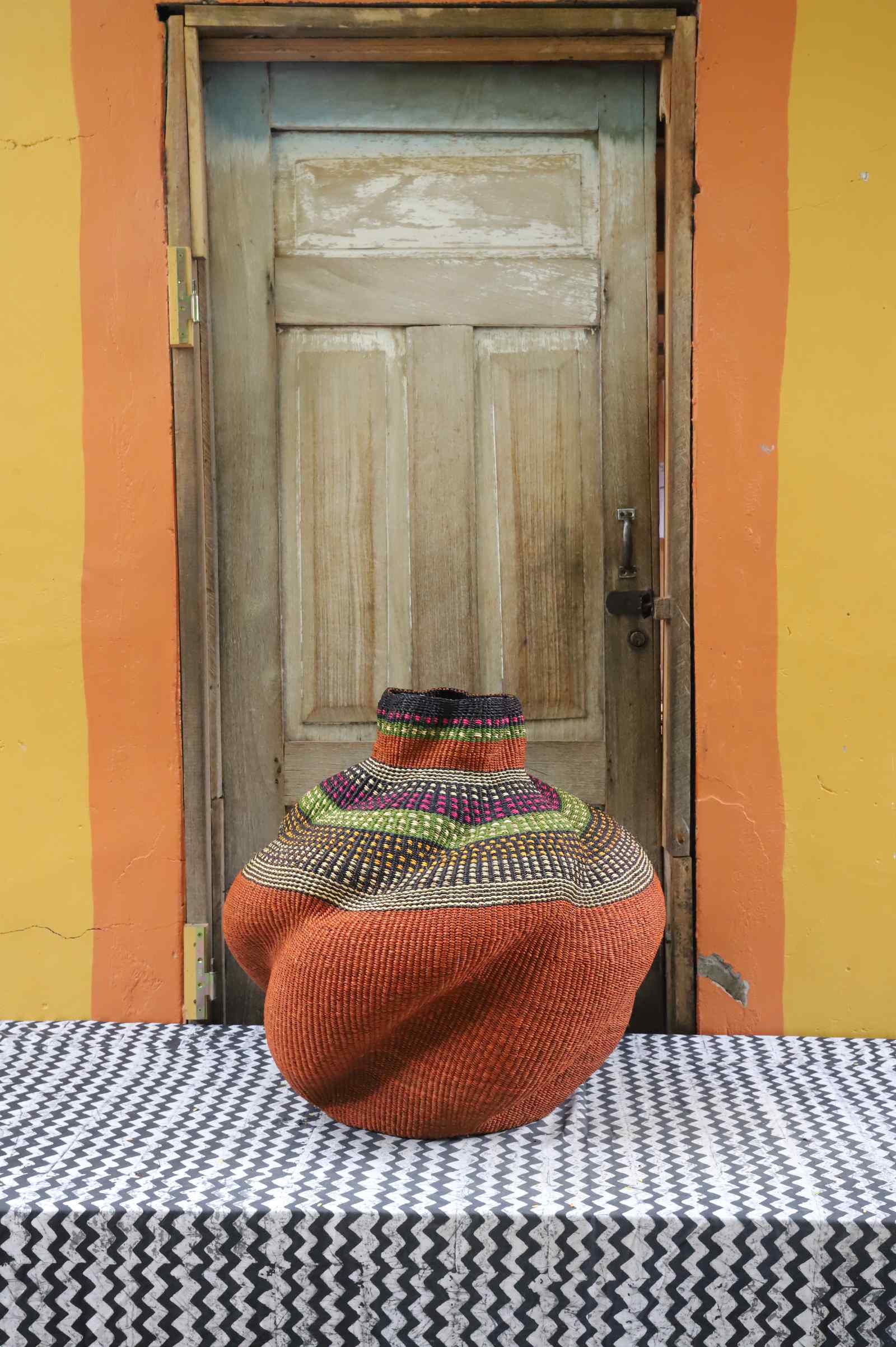 Medium handwoven Bolga art basket in a sculpted rust-orange pot with a multicolour banded shoulder.