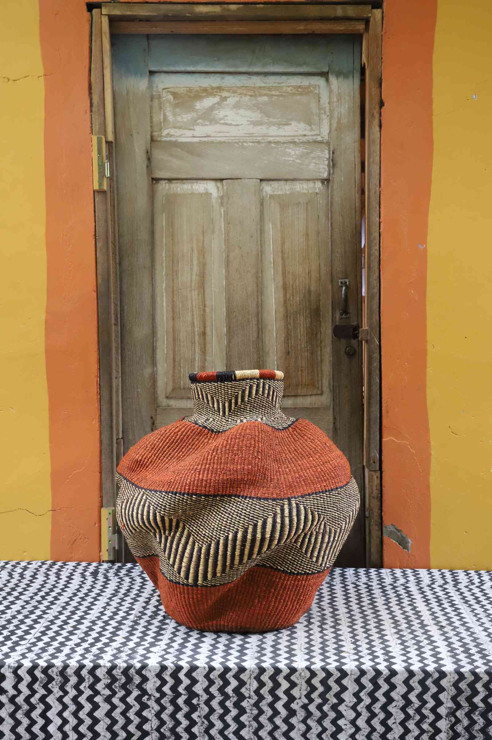 Medium handwoven Bolga art basket in a sculpted rust-orange urn with a dark spotted shoulder and multicolour rim.