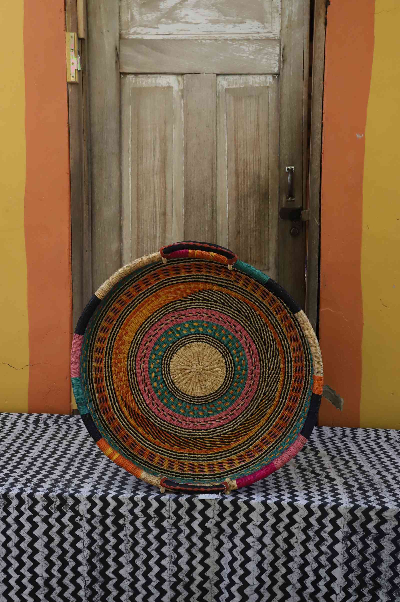 Single-weave handwoven Bolga wall tray disc in bright multicolour concentric bands with dark rim.