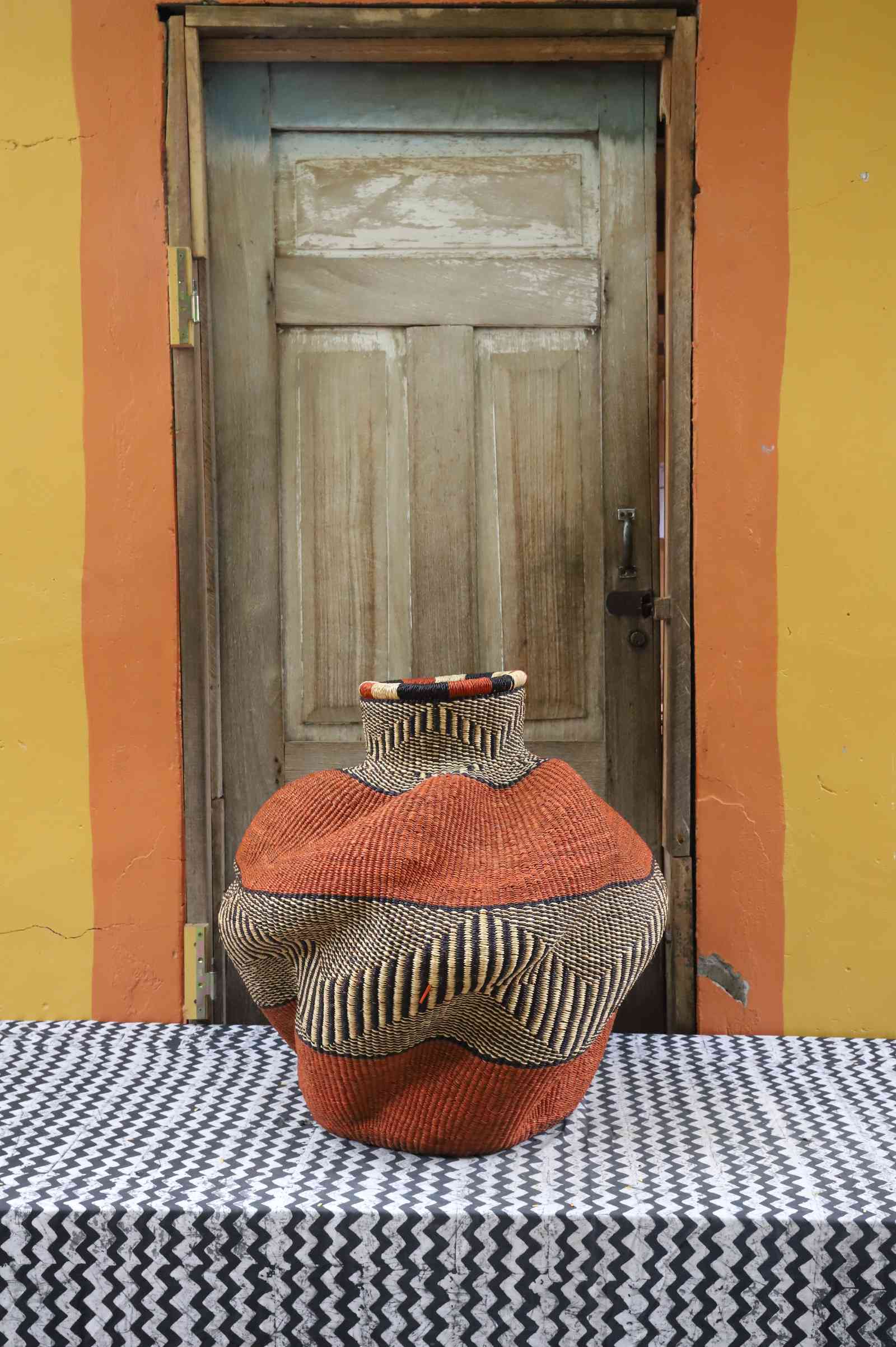 Medium handwoven Bolga art basket in rust-orange, side view showing the sculpted lobed urn form.