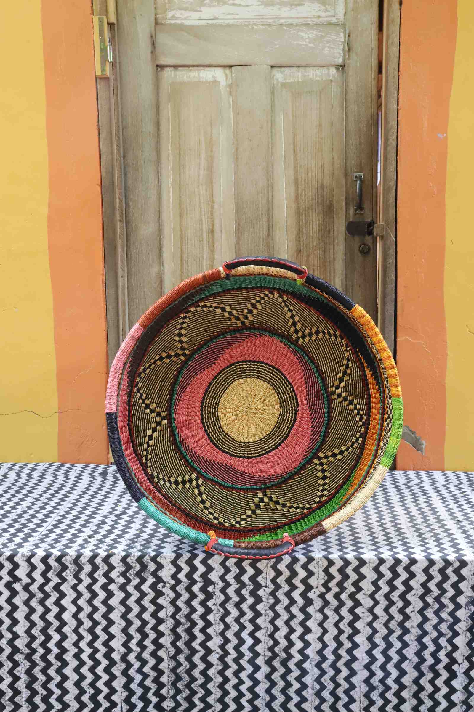 Medium handwoven Bolga wall tray disc with natural rim and concentric pink, red and orange rings.