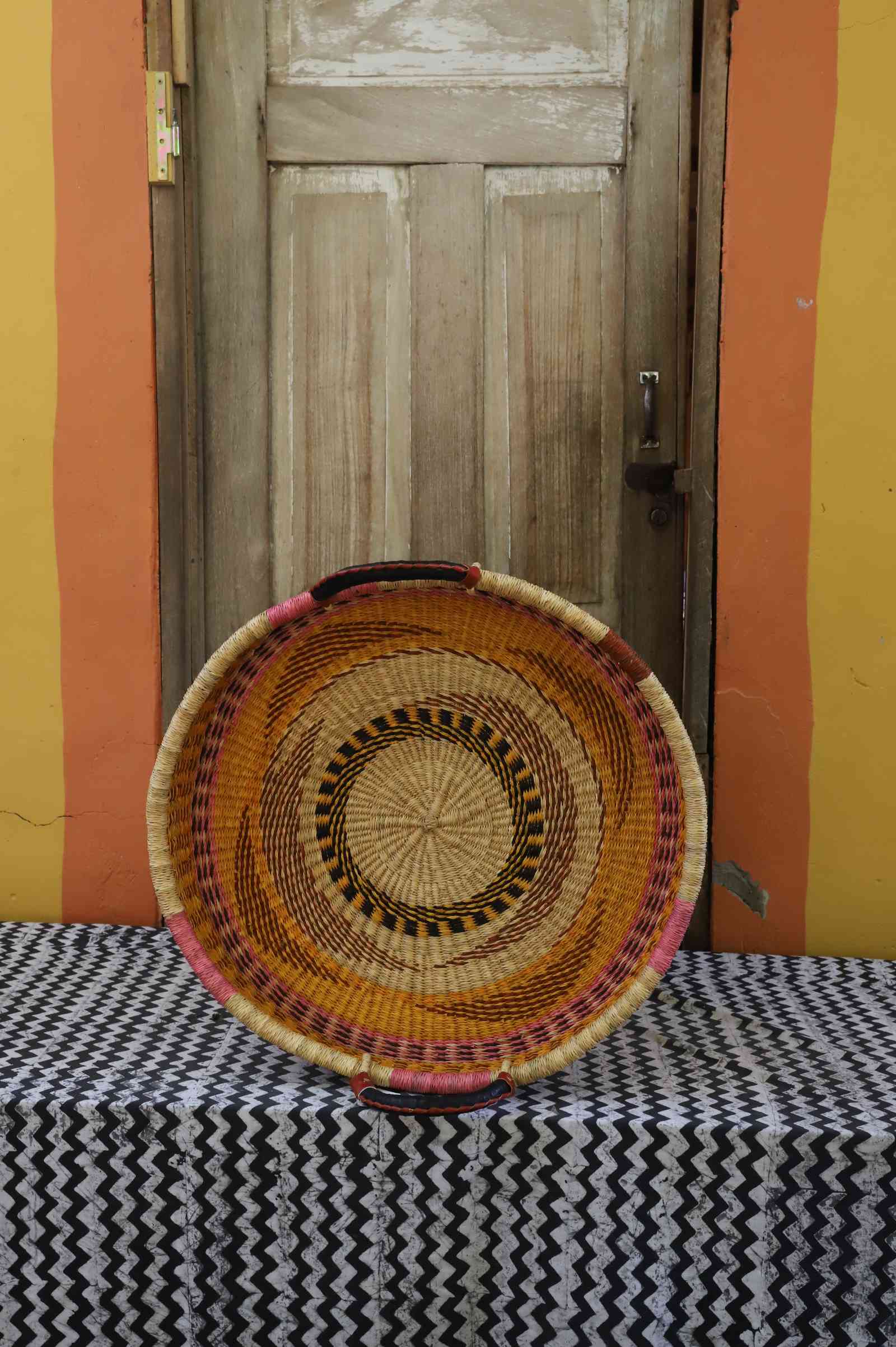 Single-weave handwoven Bolga wall tray disc with orange, red and purple concentric bands and pink handle.