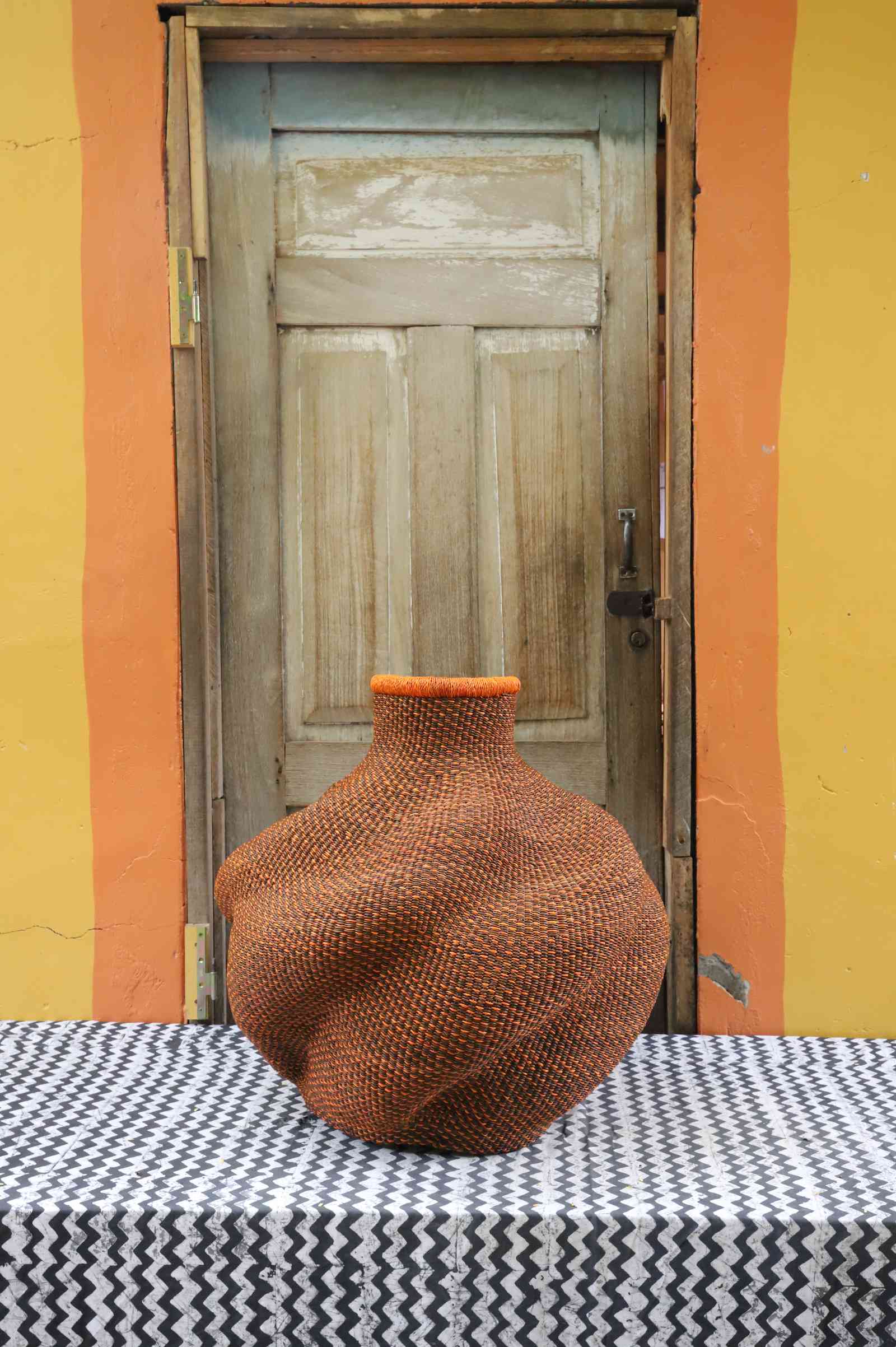 Medium handwoven Bolga art basket in a sculpted rust-red urn with a bright orange rim.