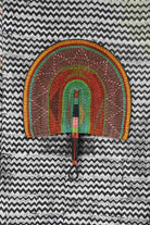 Naba Penga wall fan in natural straw with green, orange and black concentric bands, laid on a chevron cloth.