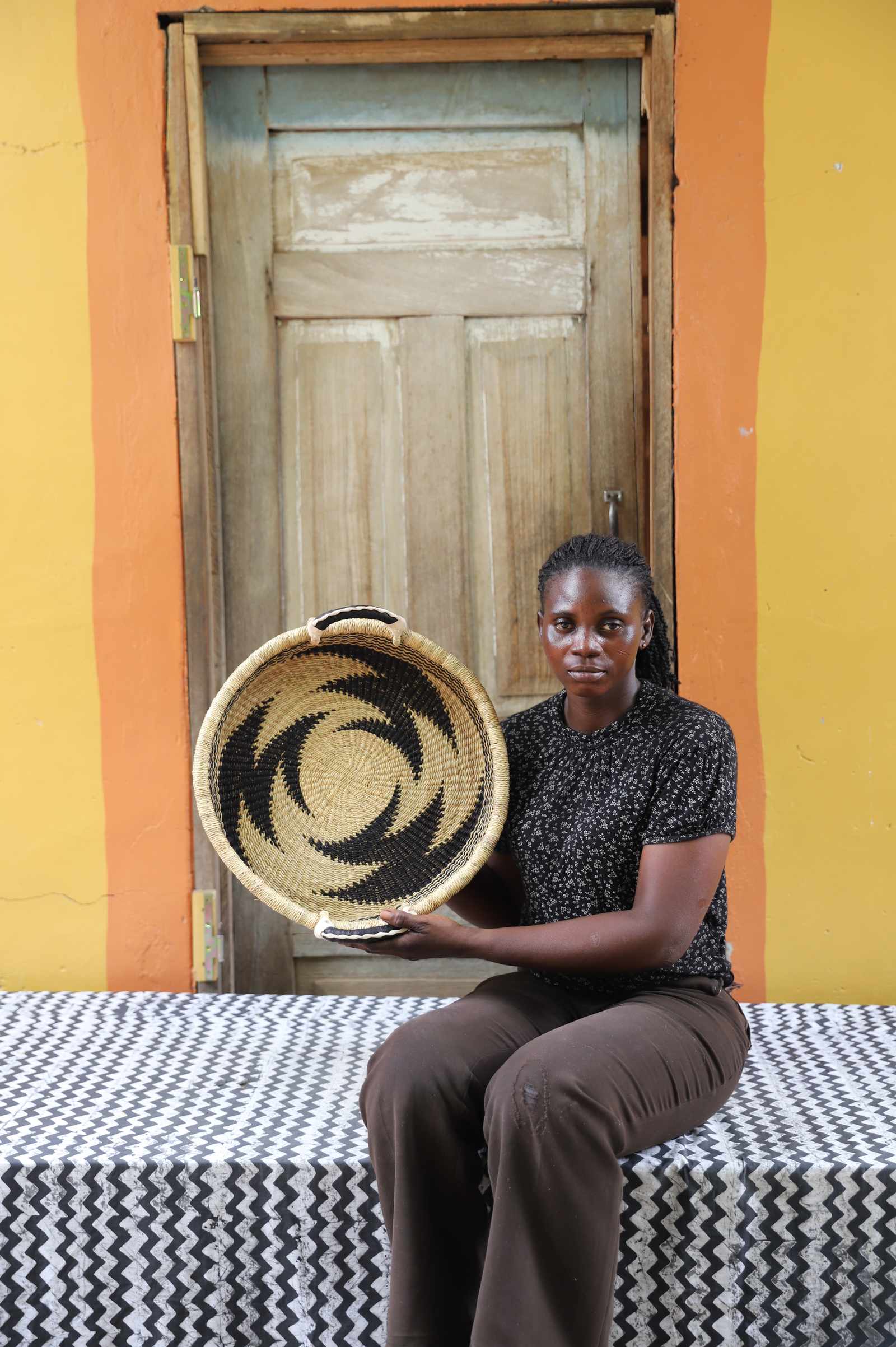 Handwoven Bolga wall tray disc with bold black star pattern, held by a seated woman in dark top.