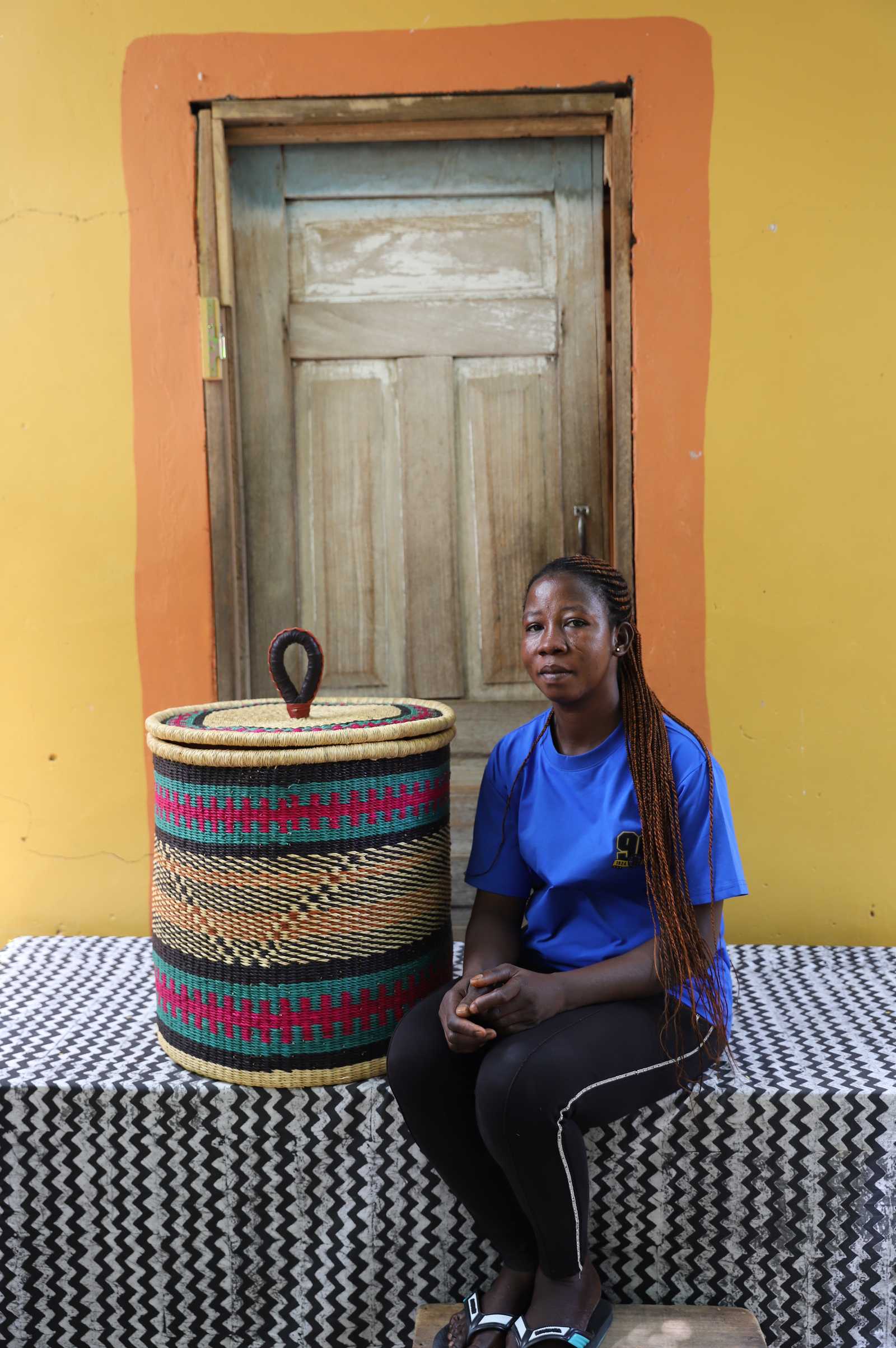 Handwoven Bolga laundry basket in fine pink, black and orange bands, beside a seated woman in blue.