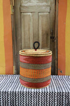 Handwoven Bolga laundry basket with coiled rim and lid in deep red with orange and yellow banded stripes.