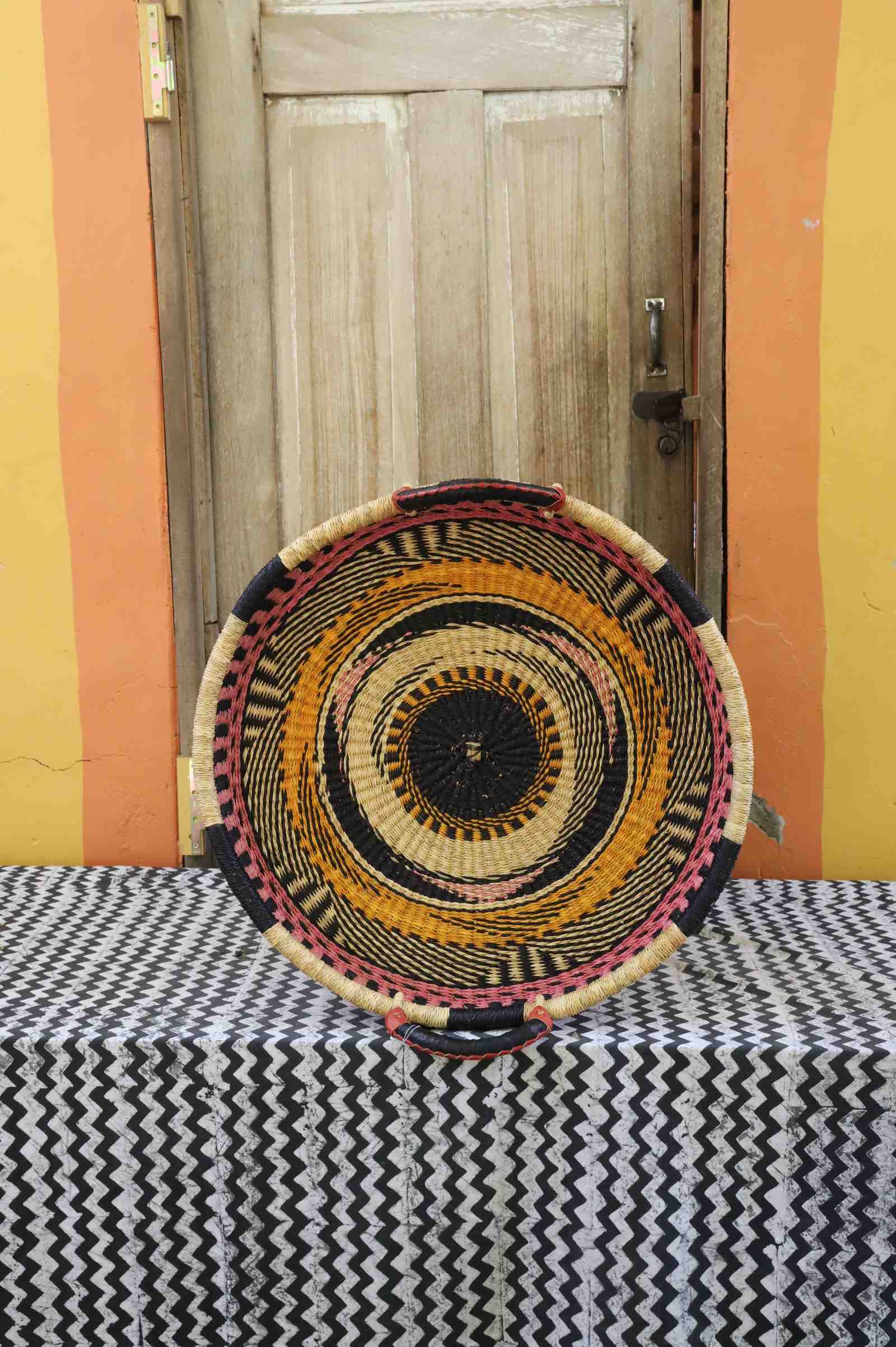 Single-weave handwoven Bolga wall tray disc with orange, black and pink concentric bands and dark centre.