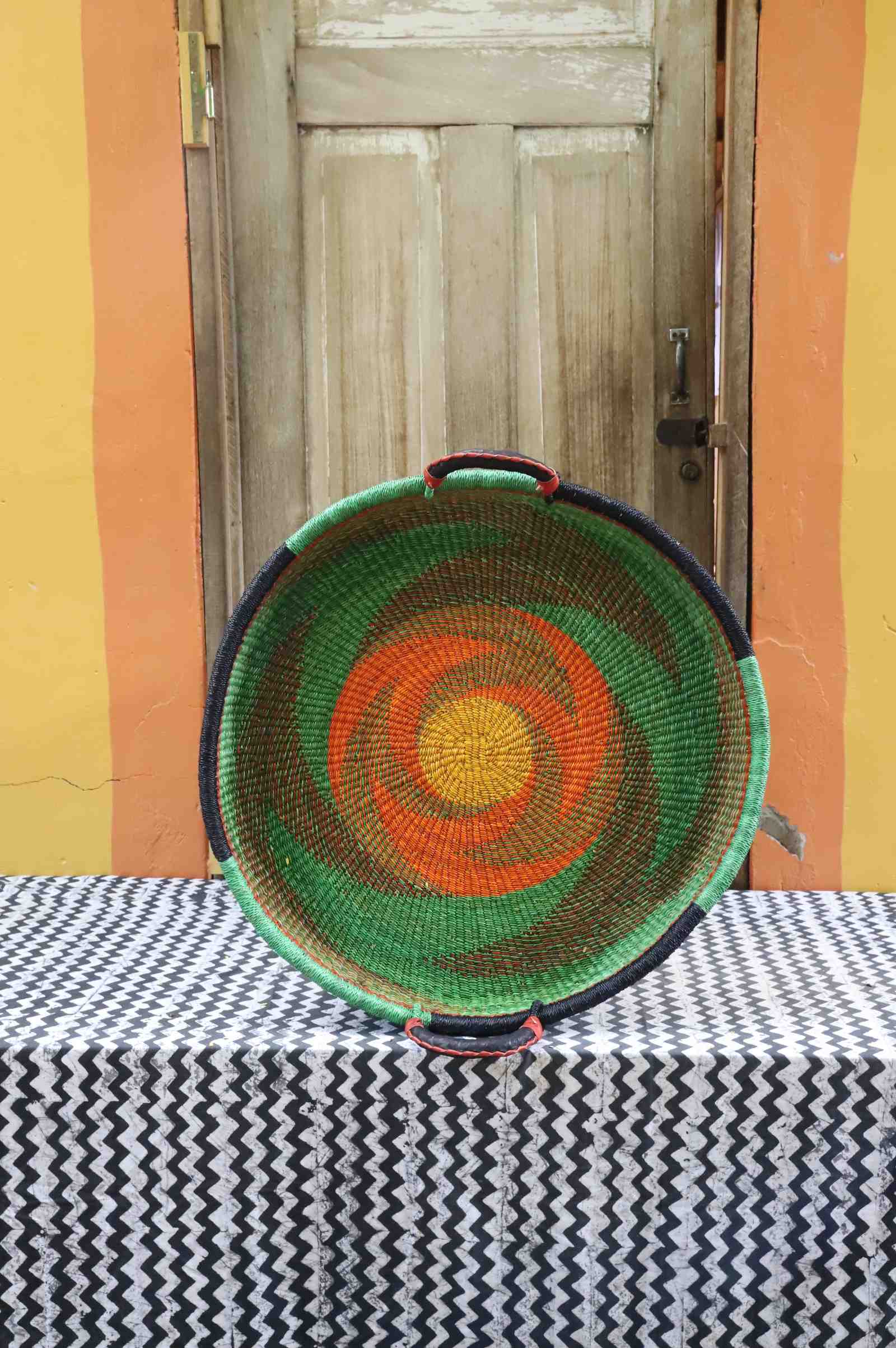 Medium handwoven Bolga wall tray disc in green with an orange pinwheel swirl and yellow centre.