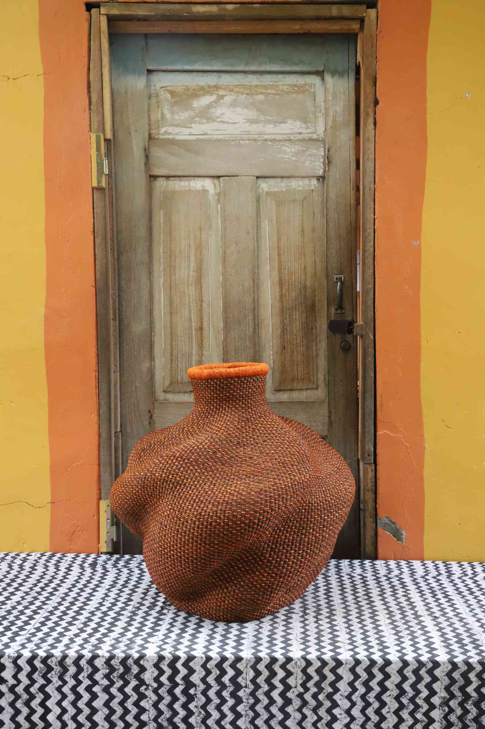 Medium handwoven Bolga art basket in rust-red, side view showing the sculpted lobed urn form.