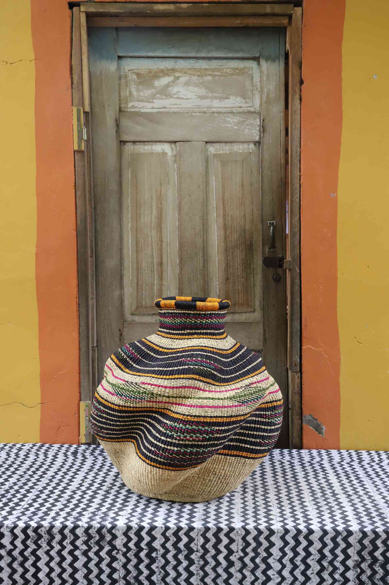 Medium handwoven Bolga art basket in a sculpted natural urn with pink, black and teal banded shoulder.
