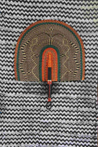 Naba Penga wall fan in natural straw with an orange and green banded border, laid on a chevron cloth.