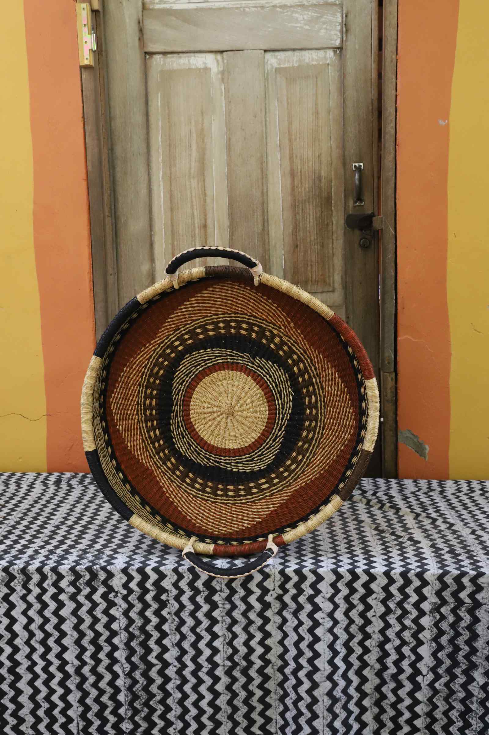 Single-weave handwoven Bolga wall tray disc with brown, red and dark banded rings and natural centre.