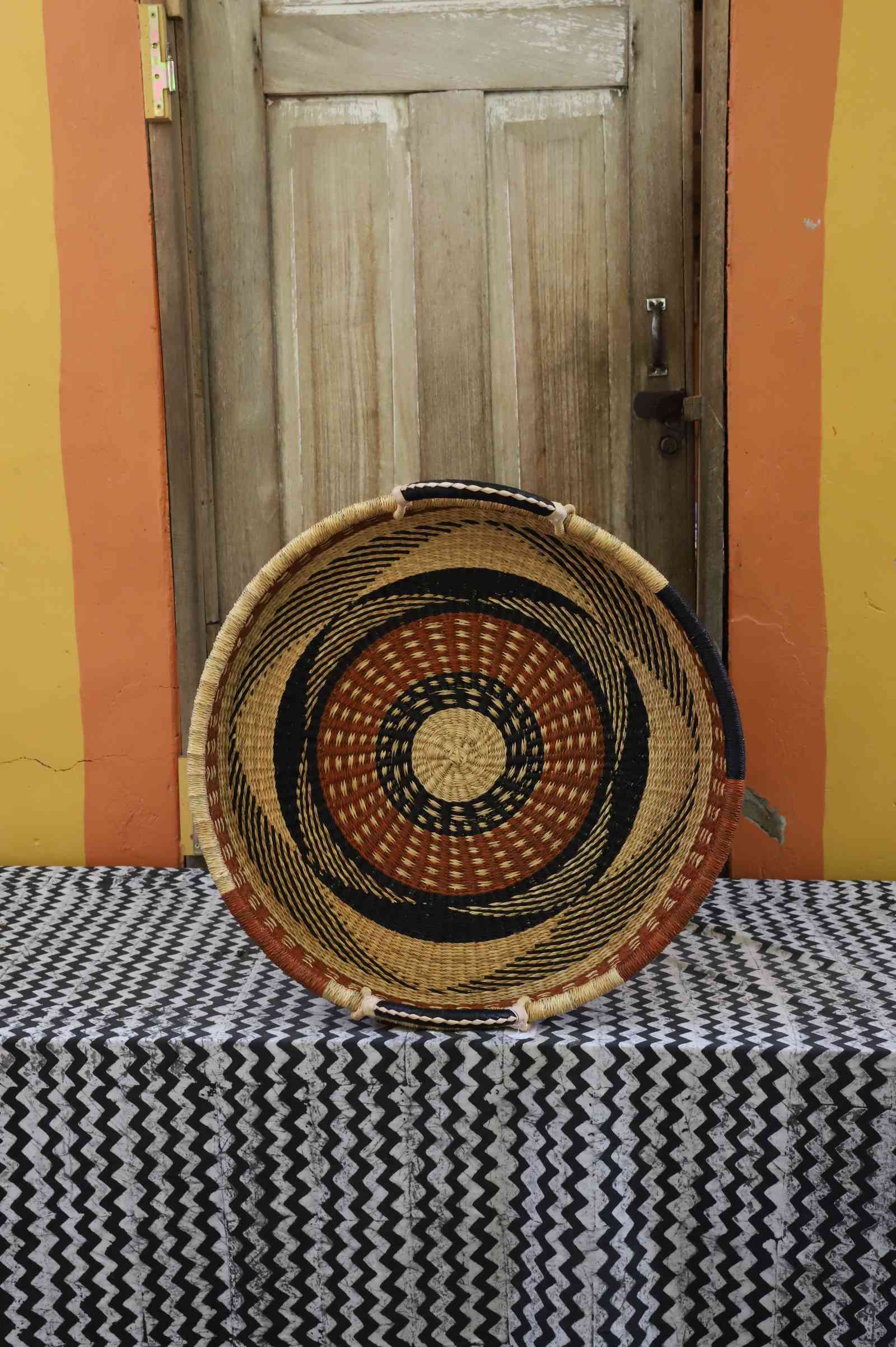 Single-weave handwoven Bolga wall tray disc with orange, black and yellow concentric bands and natural centre.