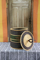 Handwoven Bolga laundry basket with lid removed, natural straw body with dark green band and arrow motif.