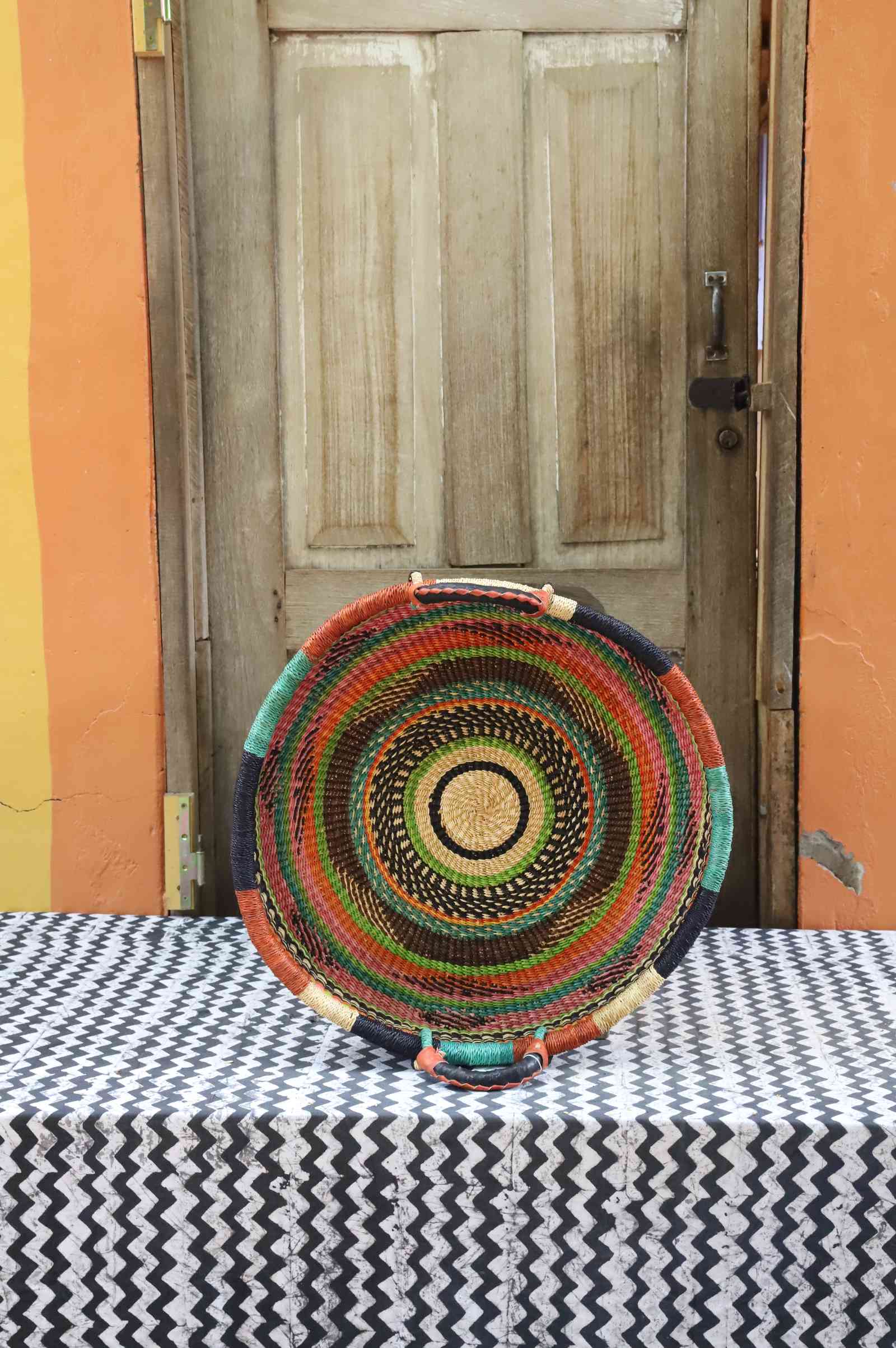 Handwoven Bolga wall tray disc with fine concentric multicolour rings on a dark body.