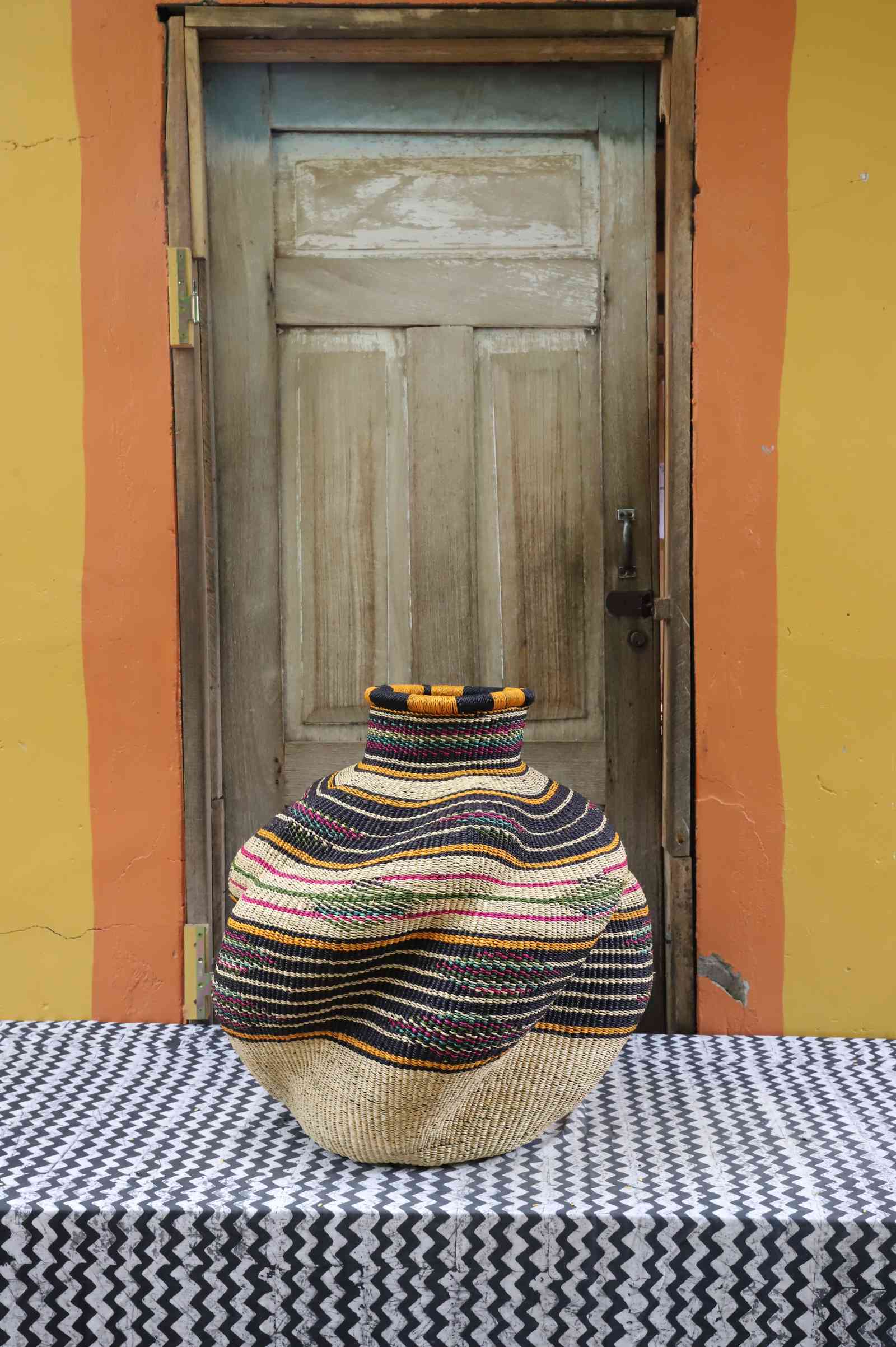 Medium handwoven Bolga art basket in natural straw with multicolour bands, side view of the sculpted urn.