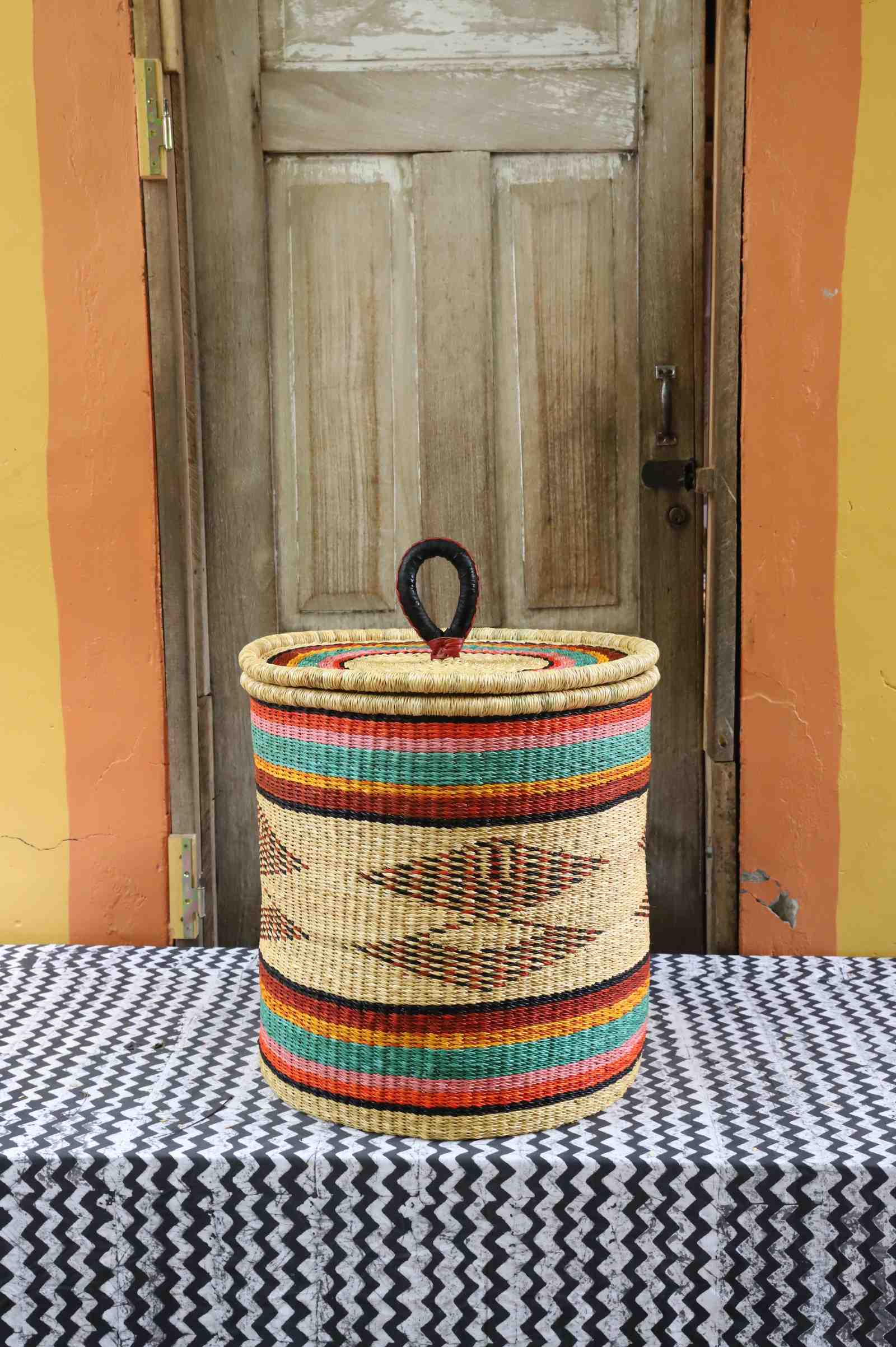 Handwoven Bolga laundry basket with coiled rim and lid in natural straw with fine multicolour bands and central motif.
