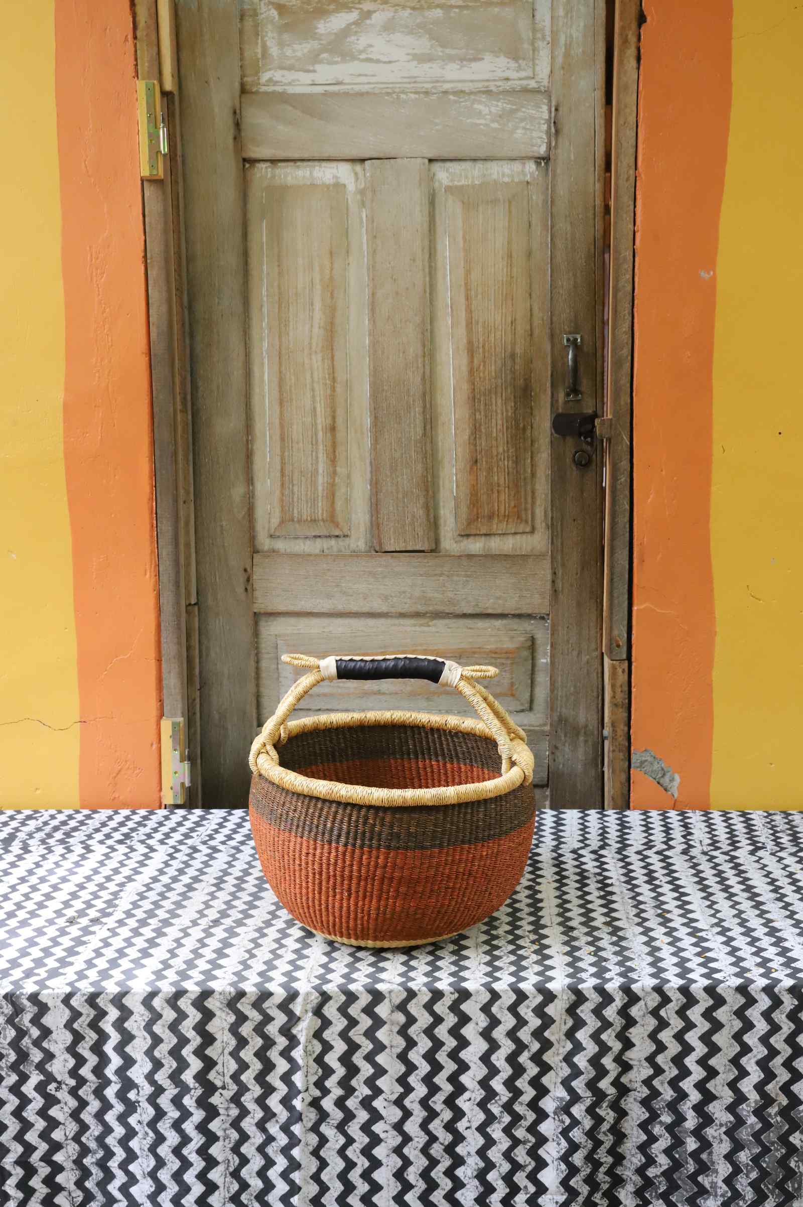 Large handwoven round Bolga shopping basket in dyed rust-orange with a dark leather-wrapped arched handle.