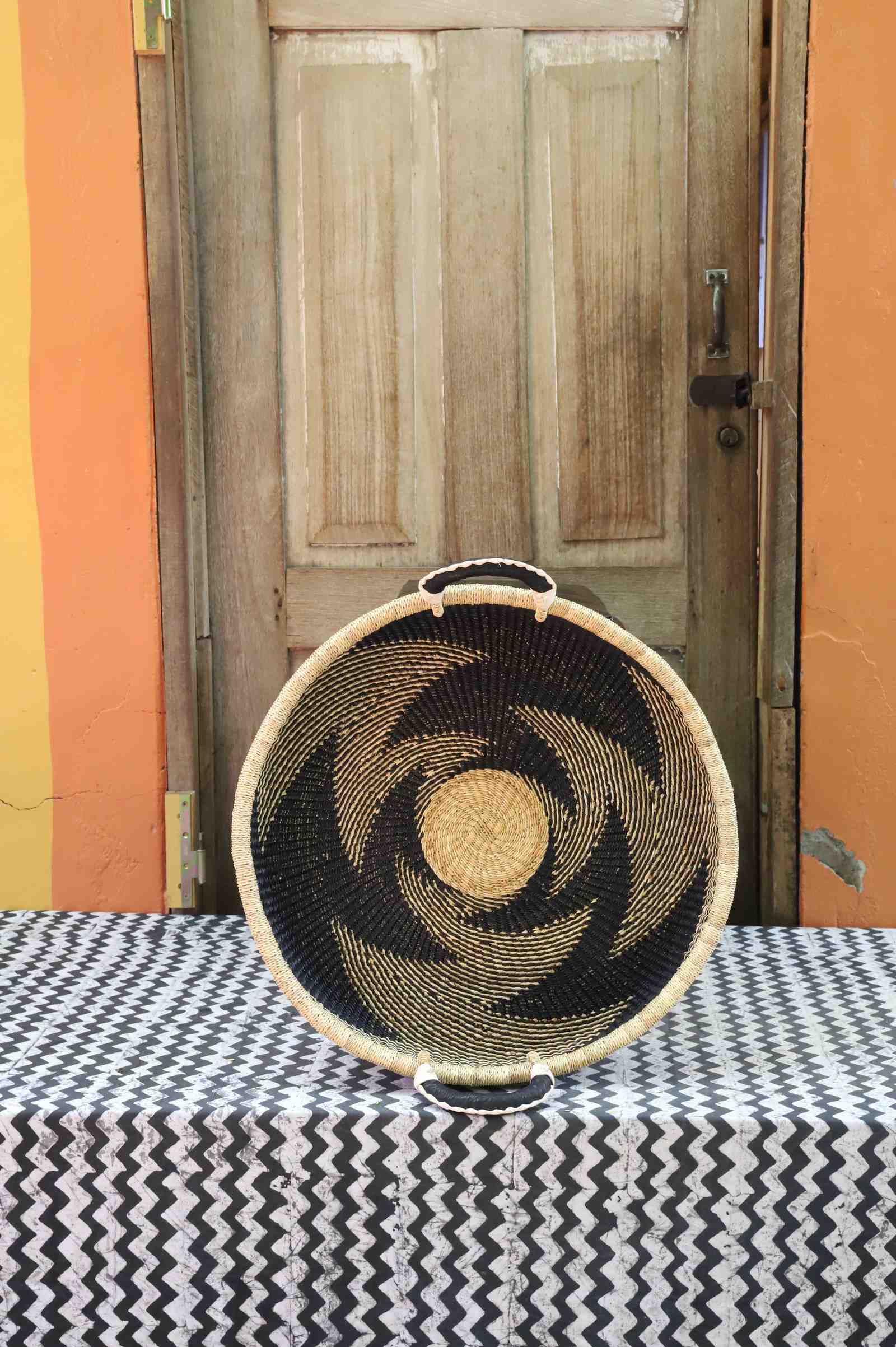 Handwoven Bolga wall tray disc in natural straw with a dark pinwheel swirl pattern.