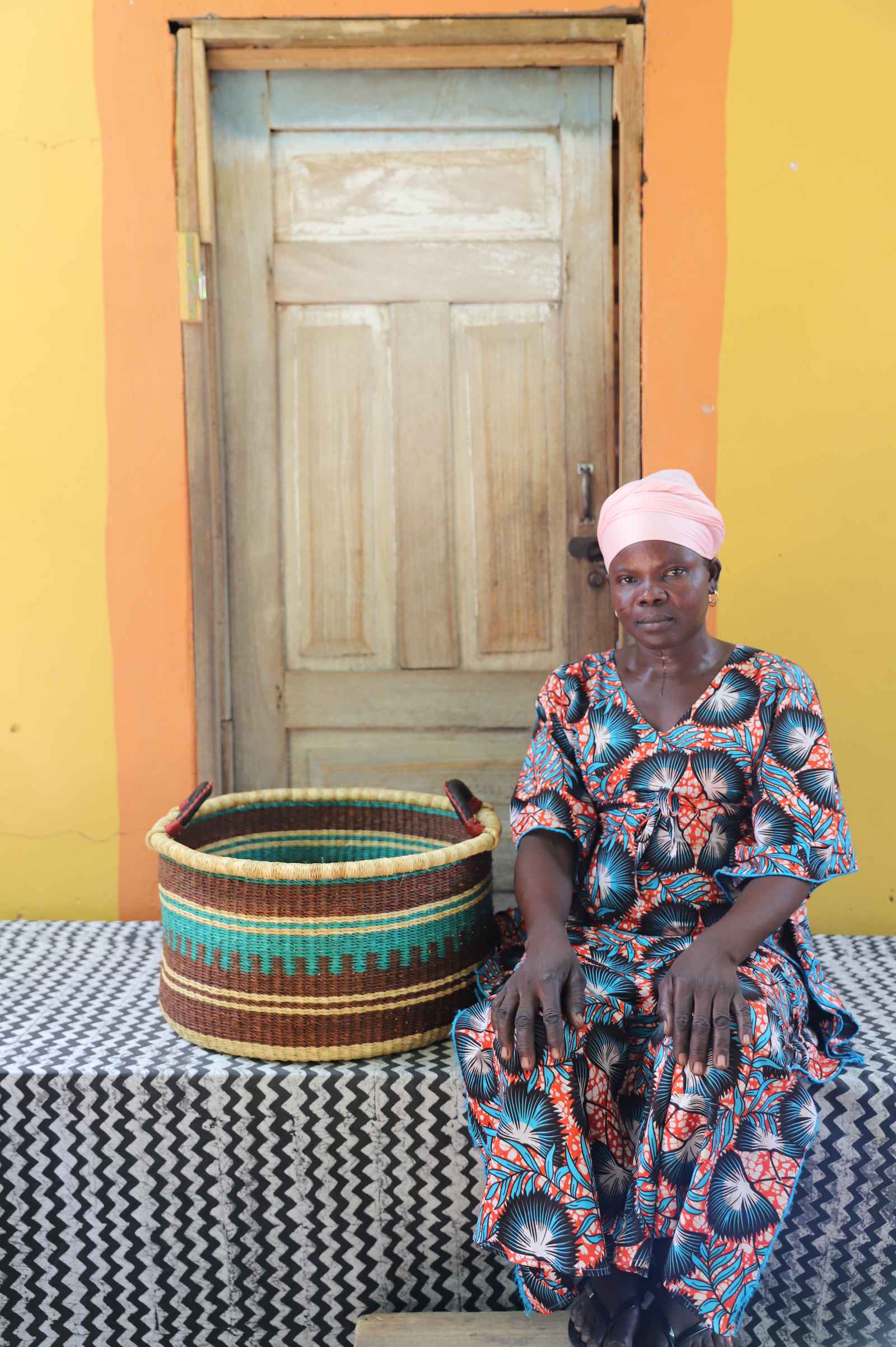 Medium handwoven Bolga storage tub in natural straw with dark banded stripes, styled beside a seated woman.