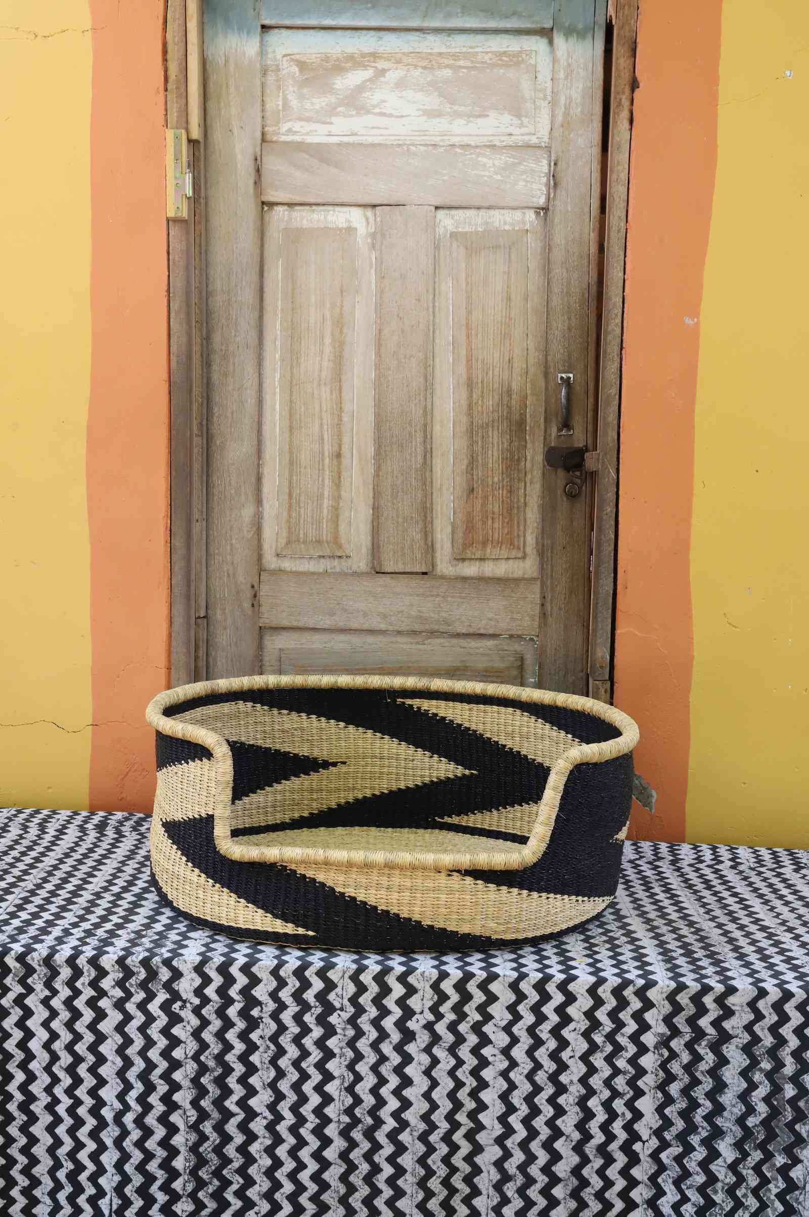 Large handwoven Bolga pet bed in natural straw with a bold black chevron and arrow pattern.