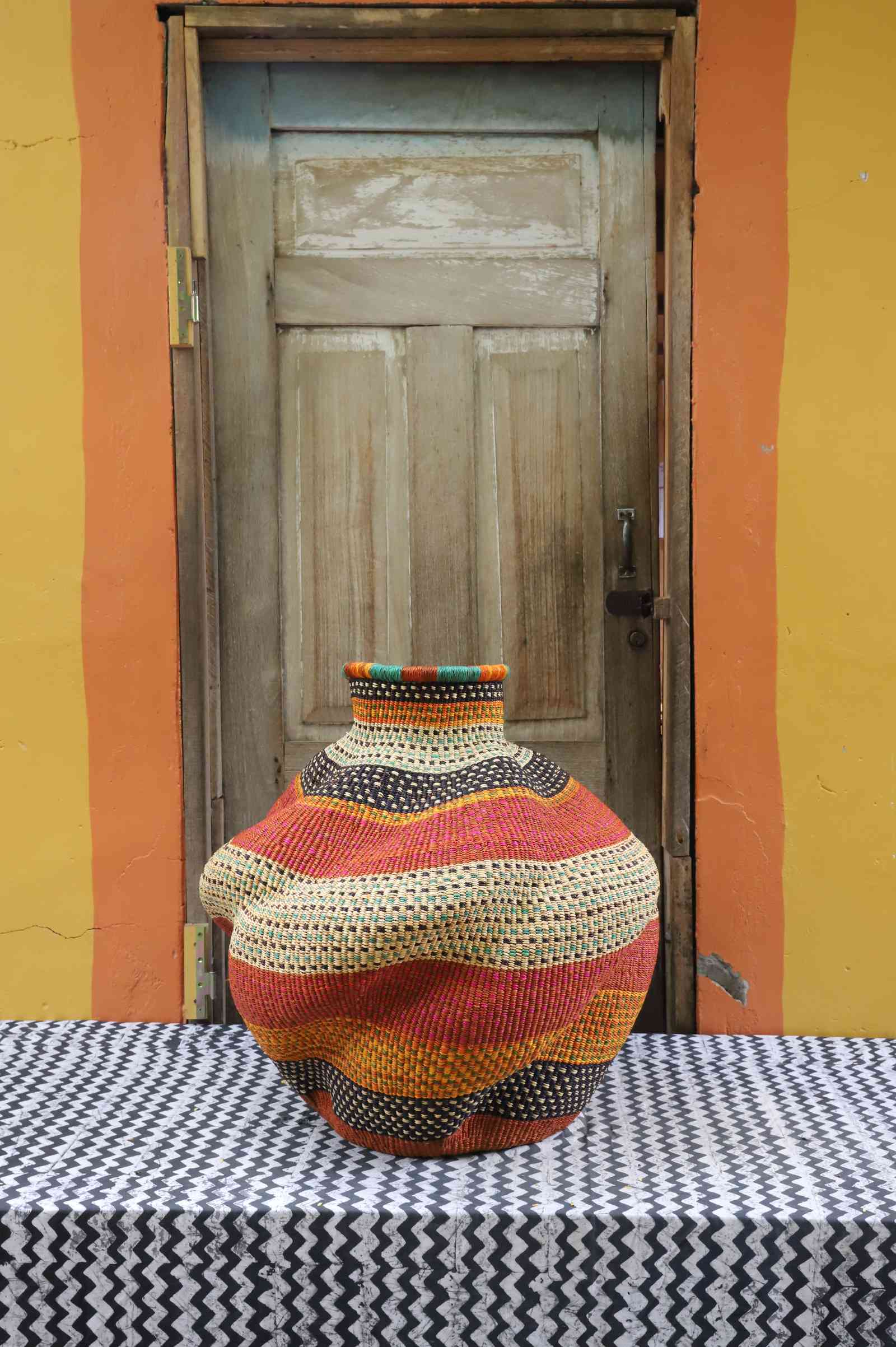Medium handwoven Bolga art basket in a rust-orange urn with dark dotted bands running through the body.