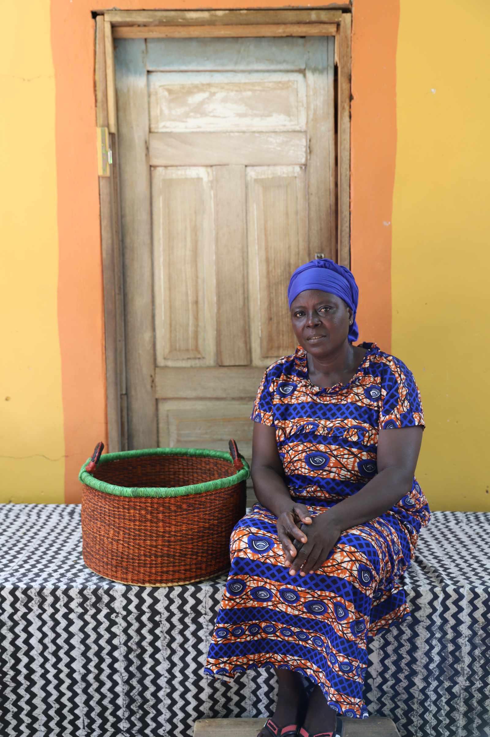 Small handwoven Bolga storage tub in natural straw with a fine green rim, styled beside a seated woman.