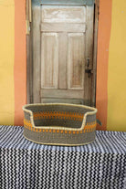 Large handwoven Bolga pet bed in natural straw with a wide orange and yellow banded central stripe.